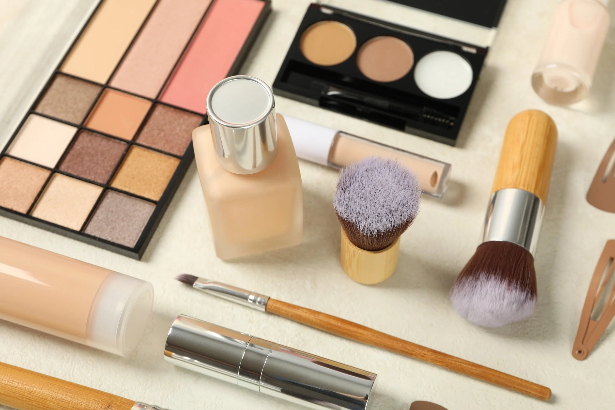 Makeup brushes, foundation bottle, eyeshadow palette, and other makeup products arranged on a surface.