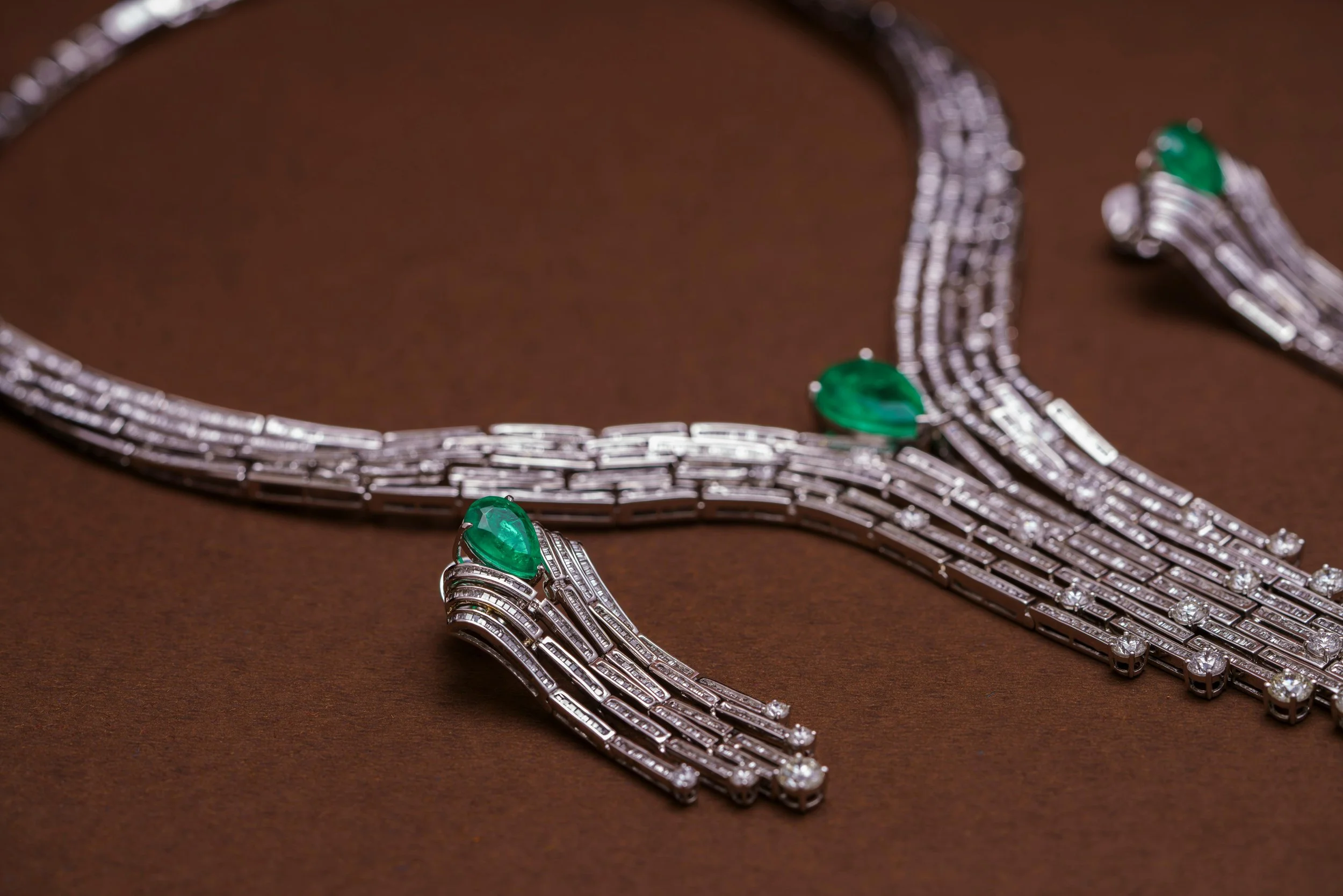A diamond and emerald jewelry set including a necklace and matching earrings displayed on a dark surface.