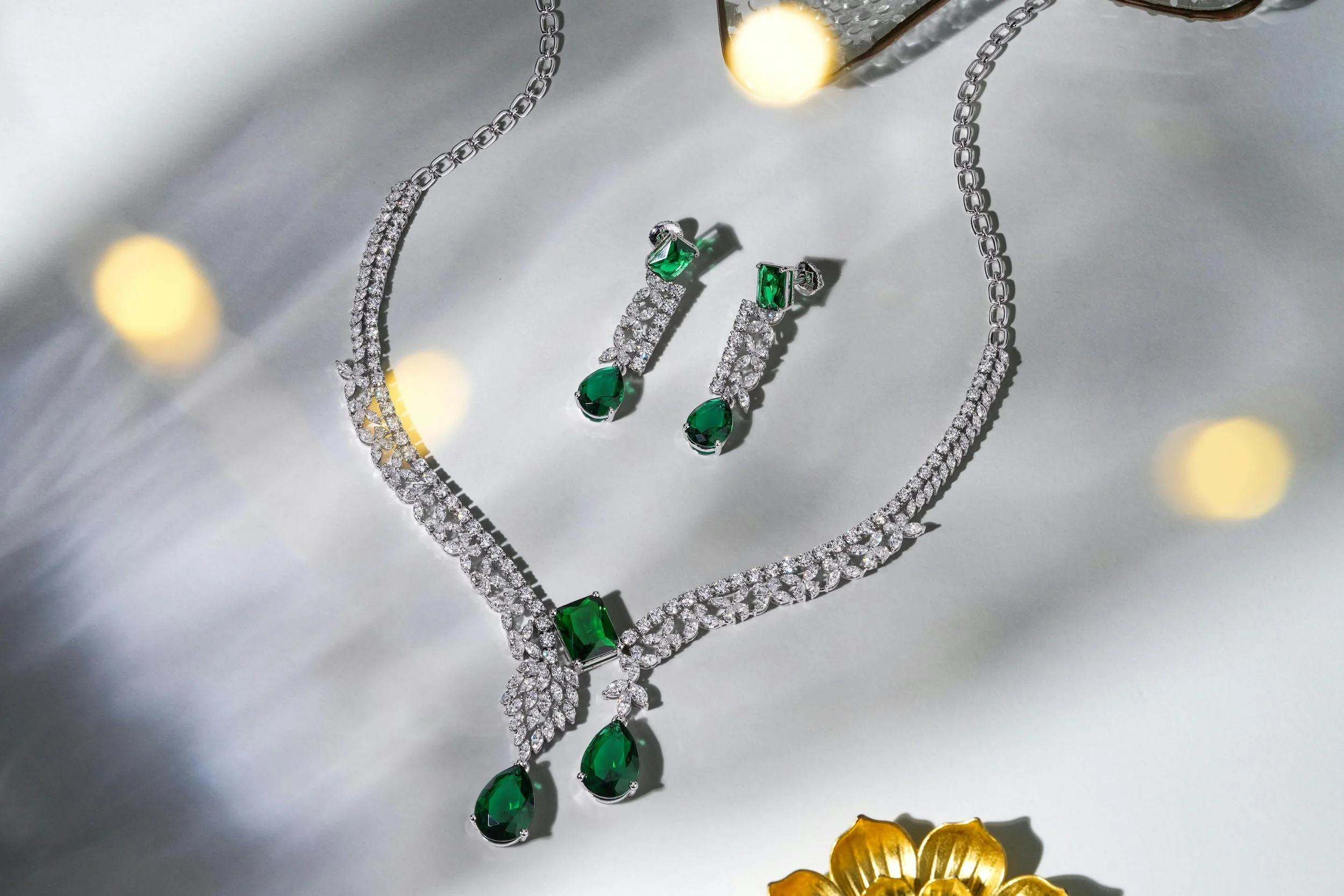 Jewelry set with a necklace and matching earrings featuring green gemstones and diamonds on a white surface.