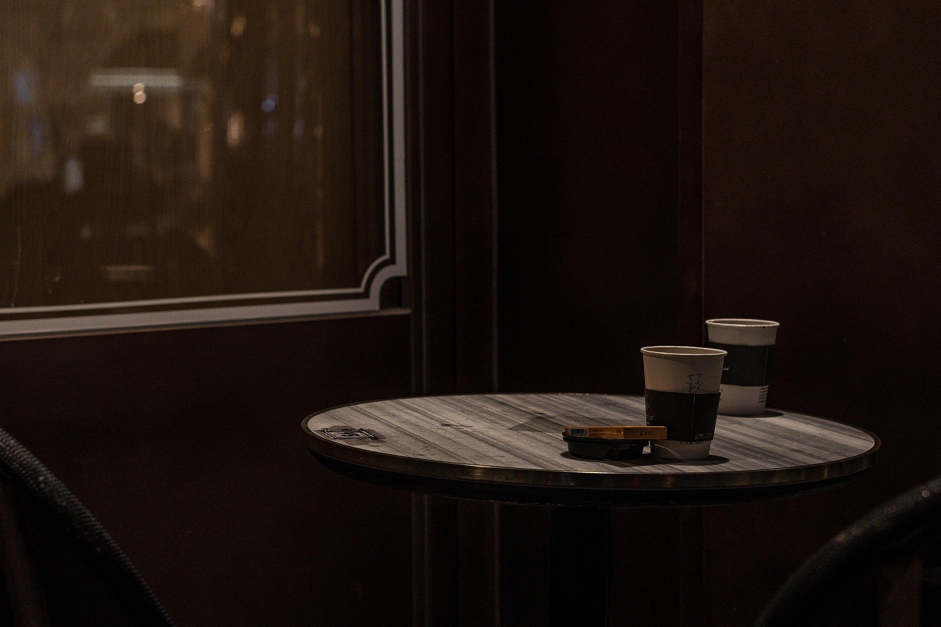 A small round table with two coffee cups and a pack of cigarettes in a dimly lit cafe or restaurant.