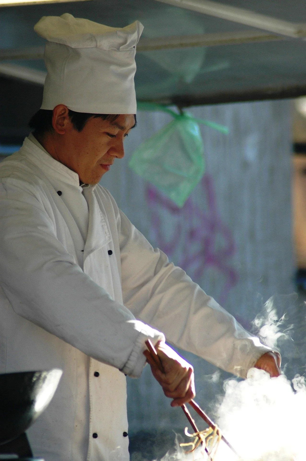 Chef in a white uniform and hat cooking with steam rising.