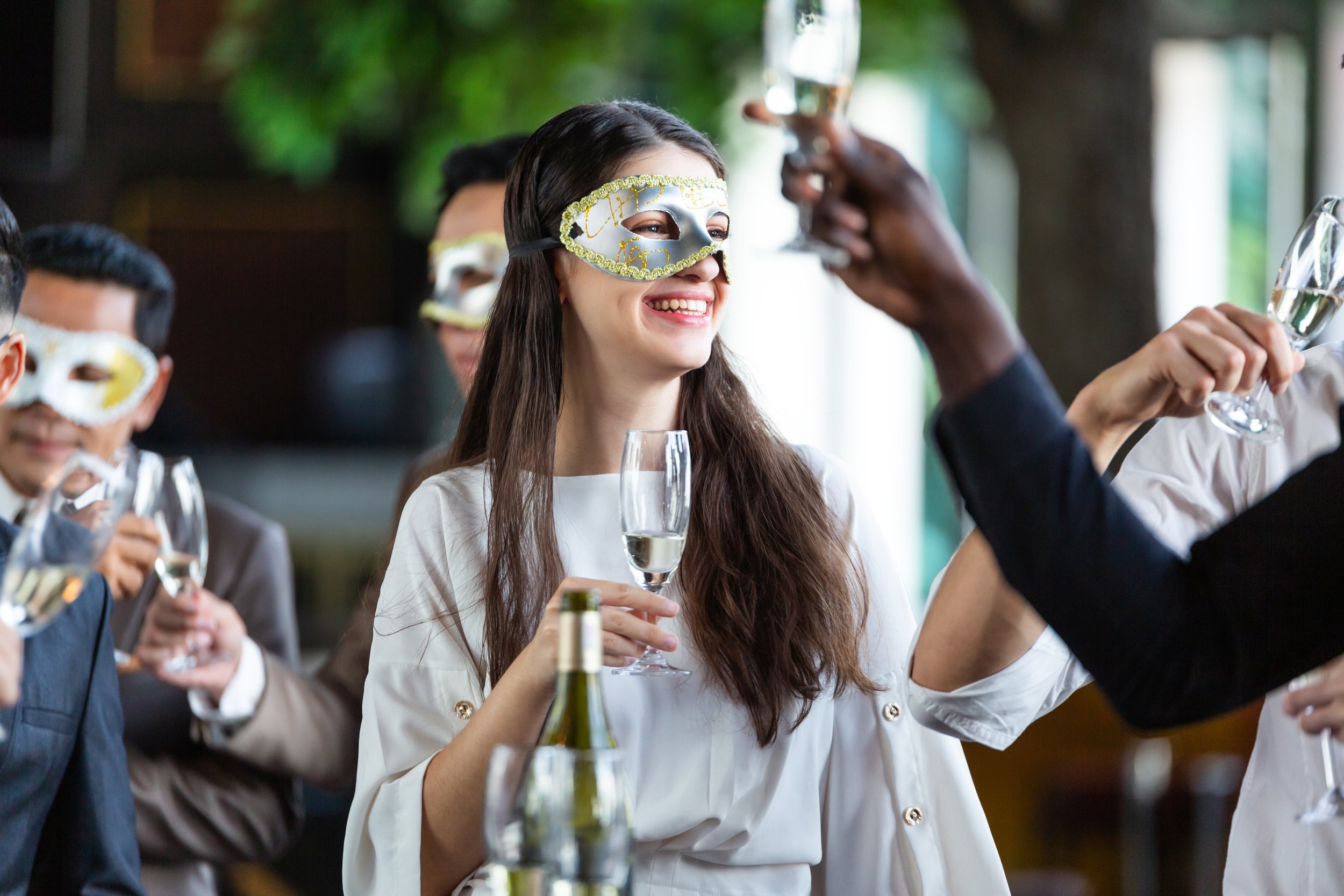People wearing masks and holding glasses of champagne at a celebration or party.