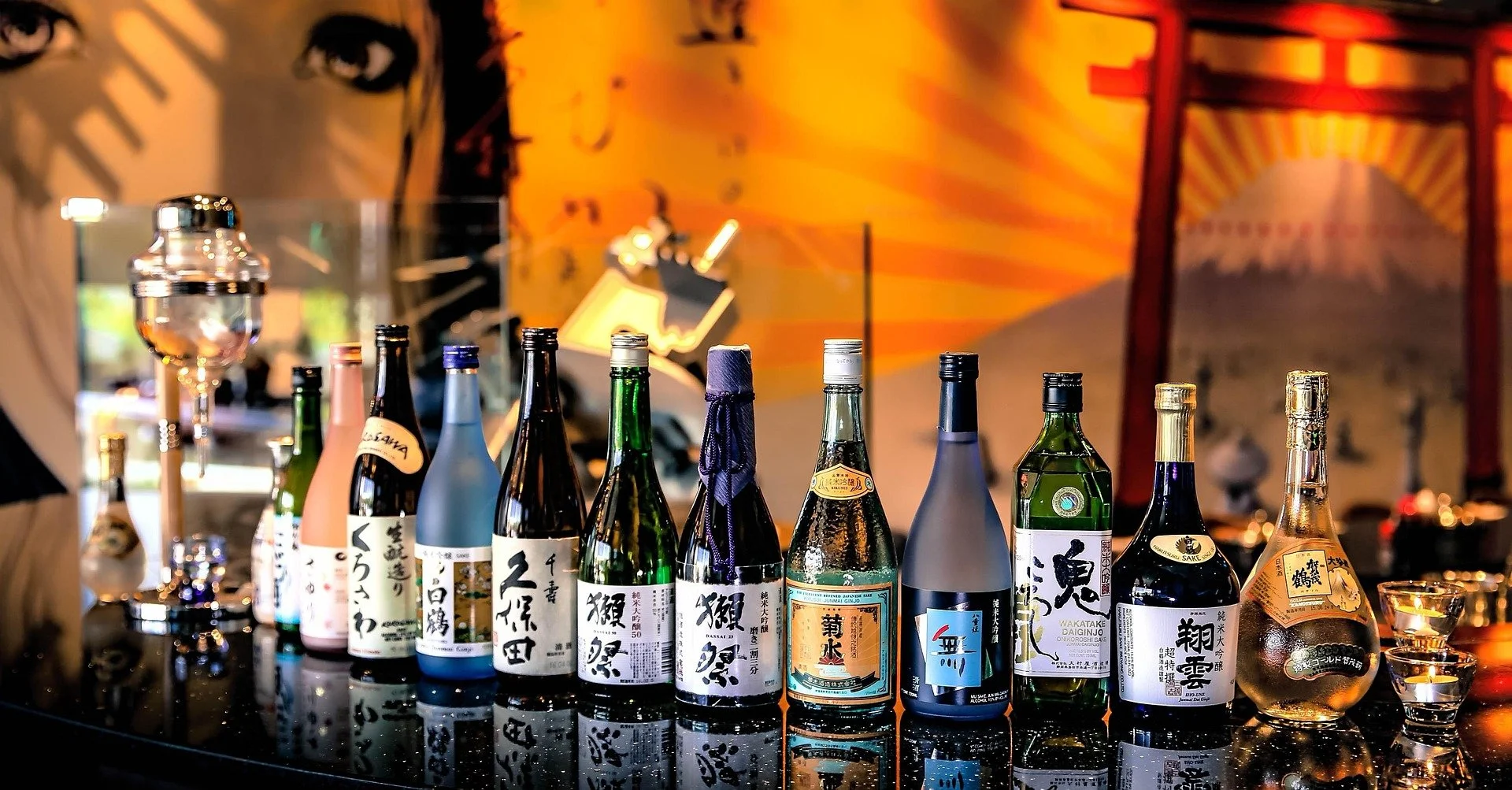 A variety of sake bottles displayed on a table in a Japanese restaurant with a colorful mural in the background.