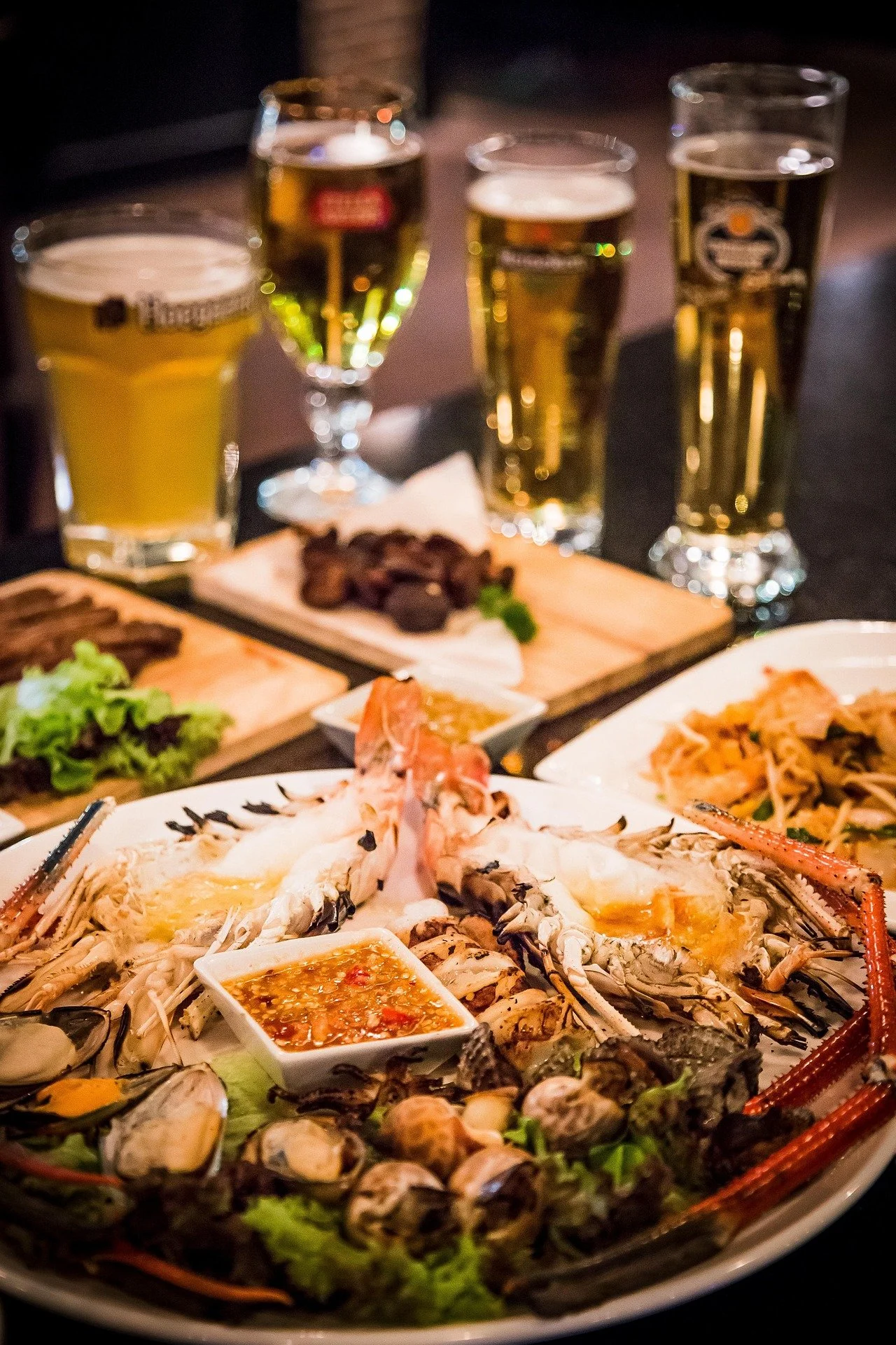 Seafood platter with lobster, oysters, and dipping sauces in front of a table of drinks, beers, and small appetizers.