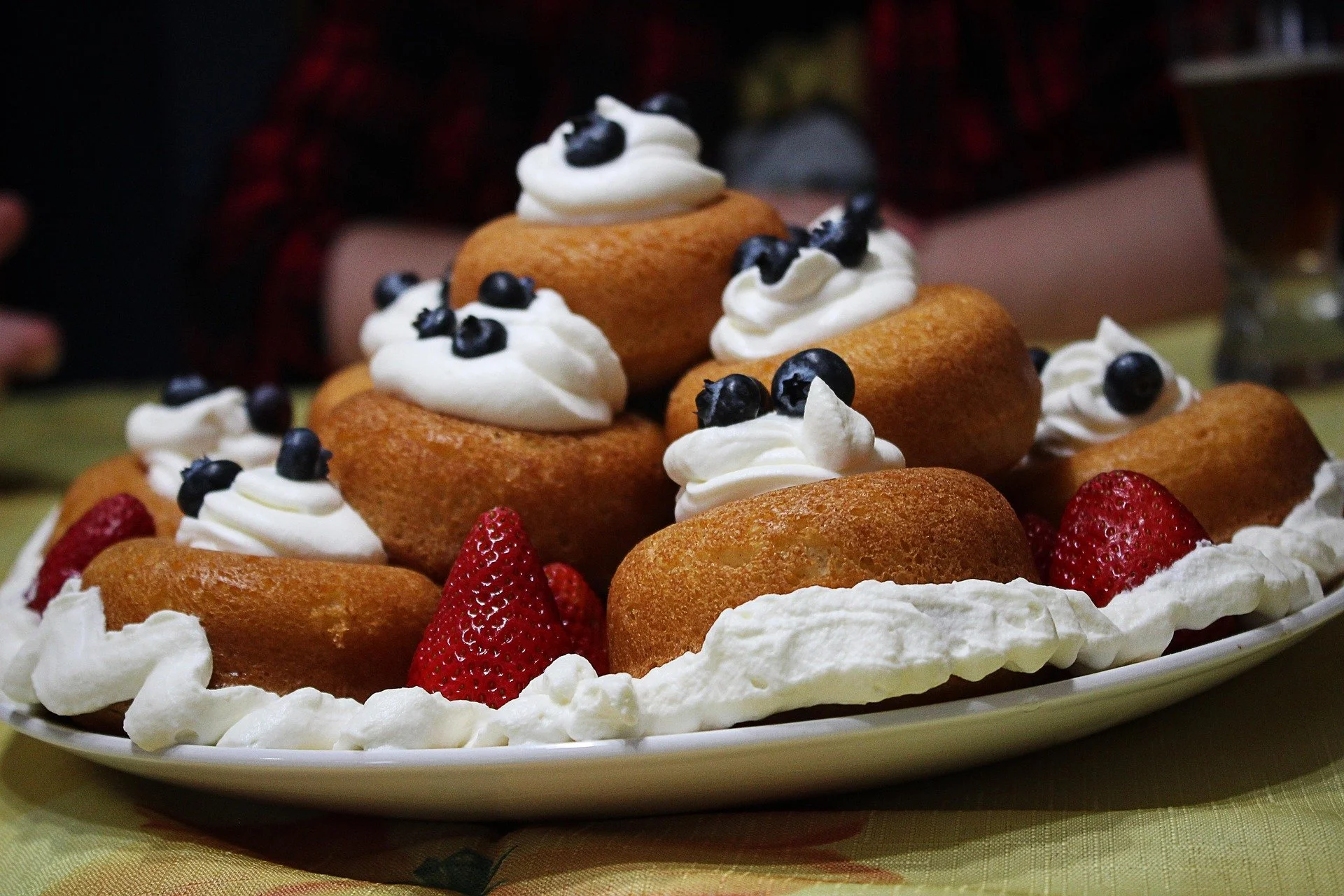 Plate of cupcakes decorated with whipped cream and blueberries, garnished with strawberries, on a table.