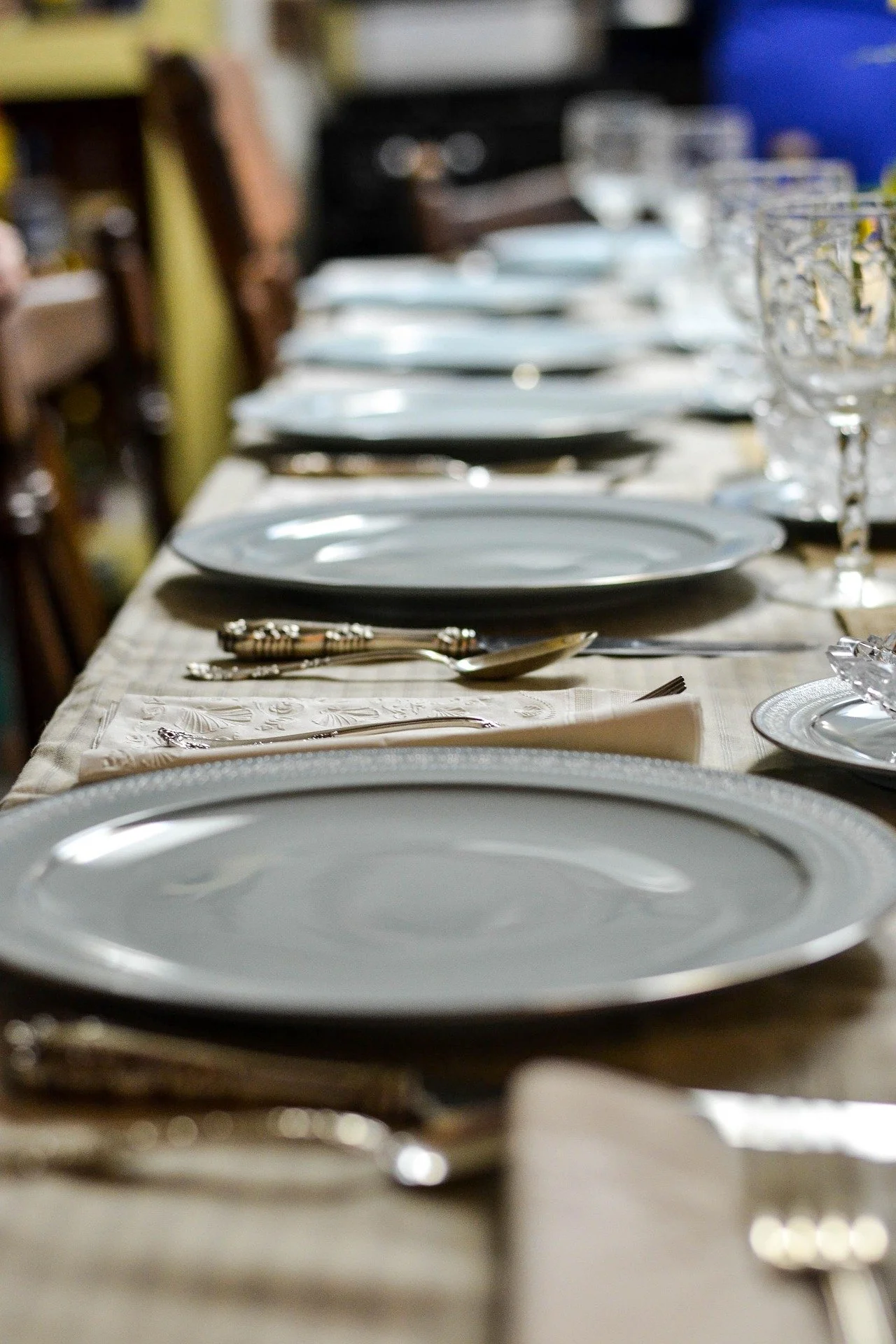 A long dining table set with white plates, silverware, napkins, and empty glassware for a formal meal.