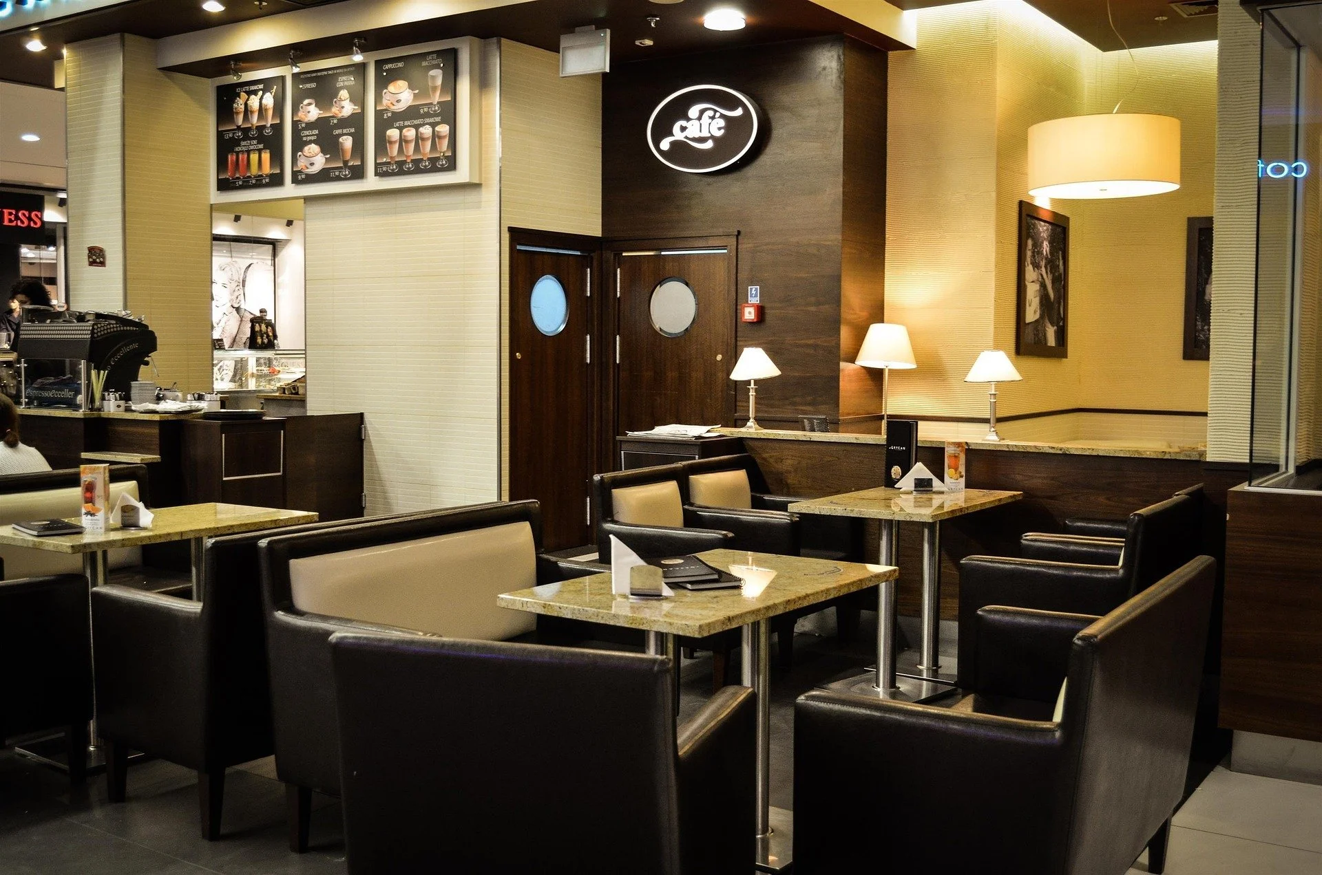 Interior of a cafe with tables, chairs, lamps, and a menu board displaying coffee drinks.