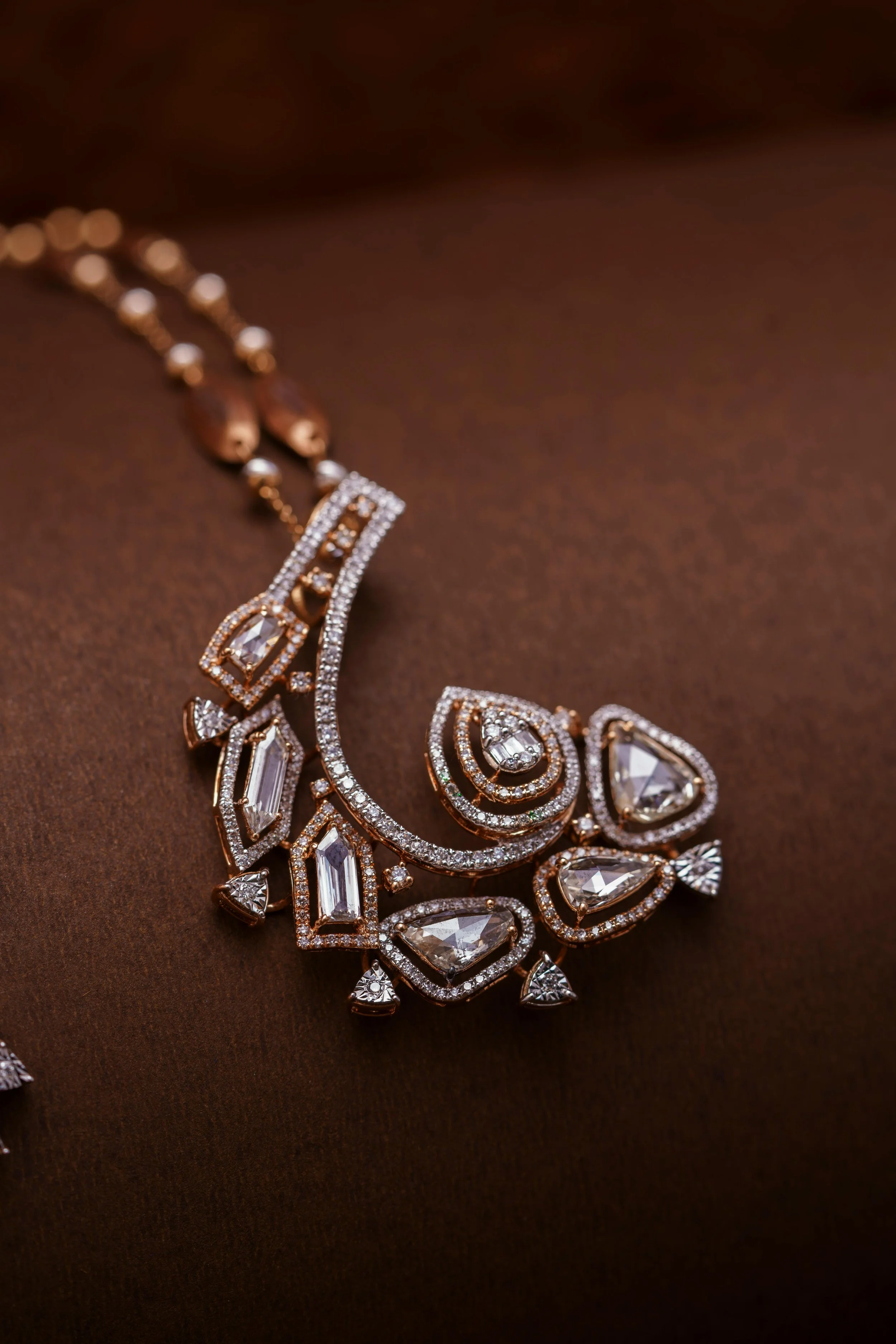 A gold necklace with diamond embellishments on a brown surface.