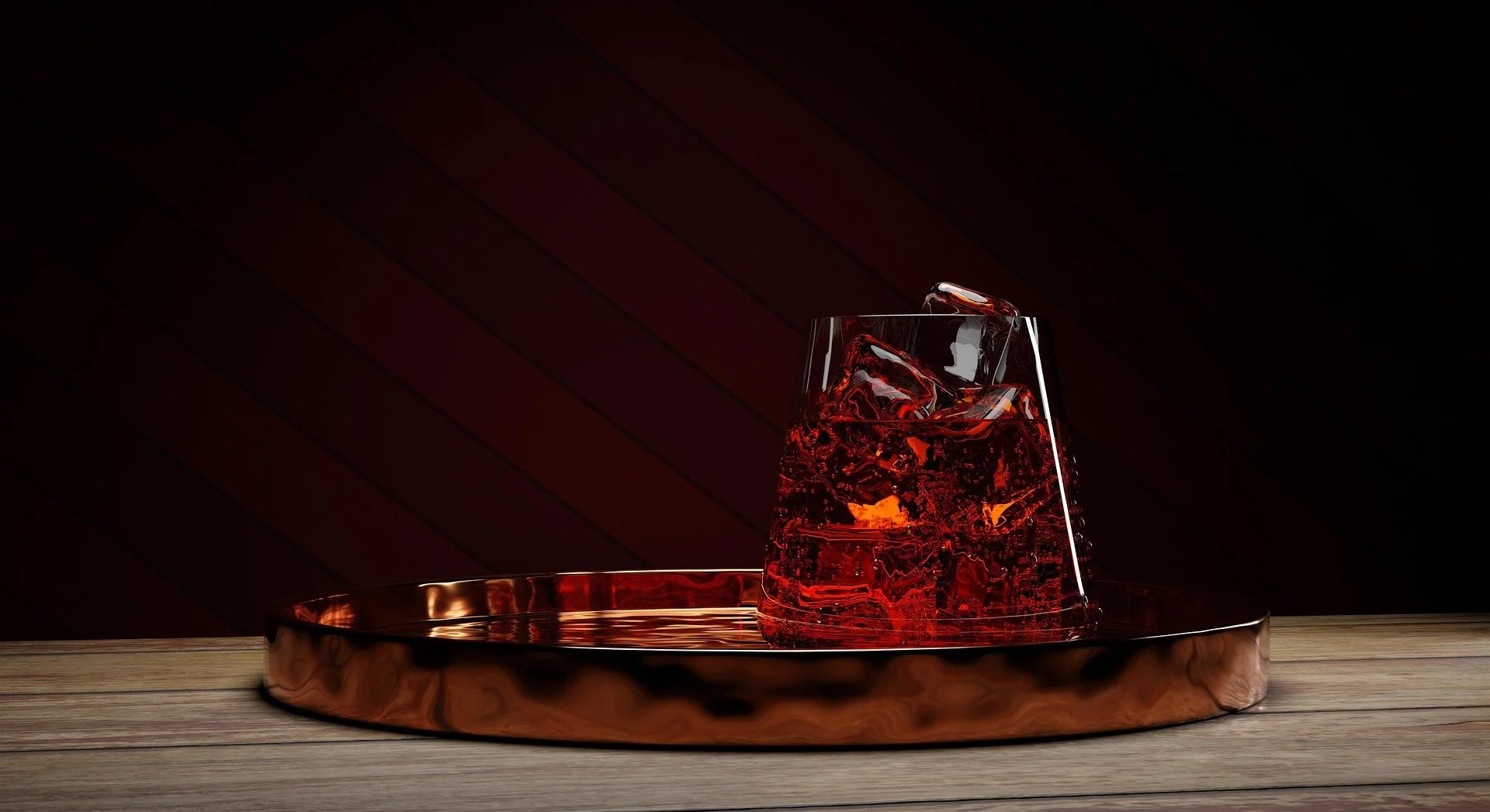 A glass with a dark red beverage and ice cubes on a shiny copper tray placed on a wooden surface.