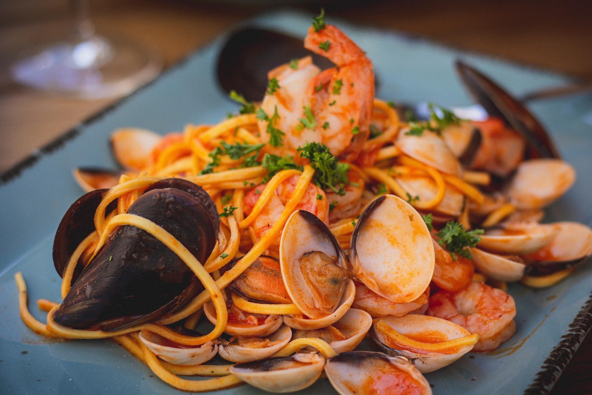 Seafood pasta with shrimp, mussels, and clams garnished with chopped parsley on a blue plate.