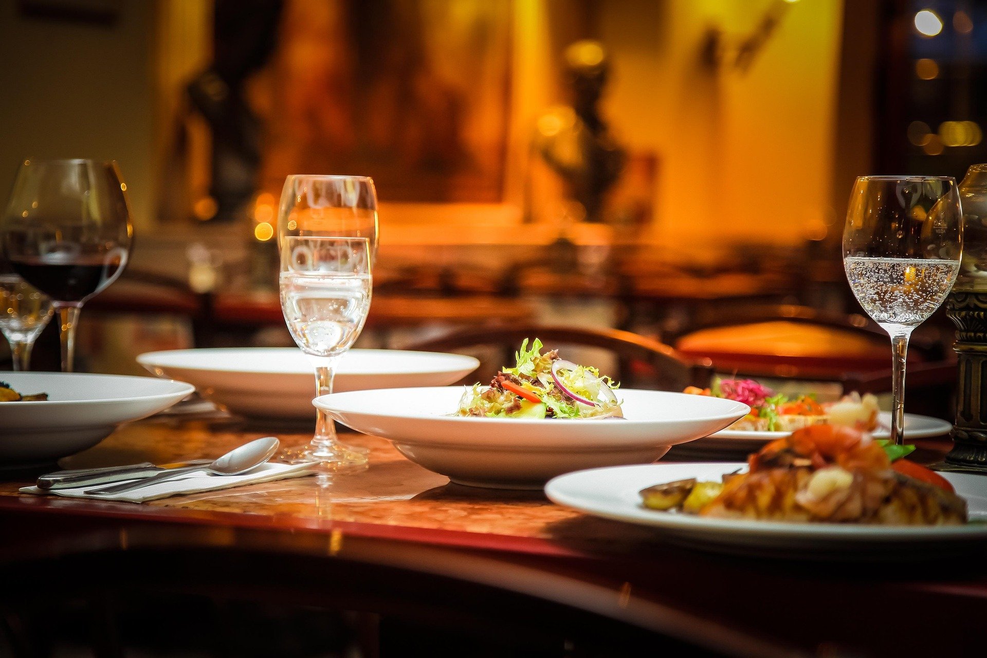 Elegant dining table set with plates of salad and other dishes, glasses of water and red wine, in a warmly lit restaurant.