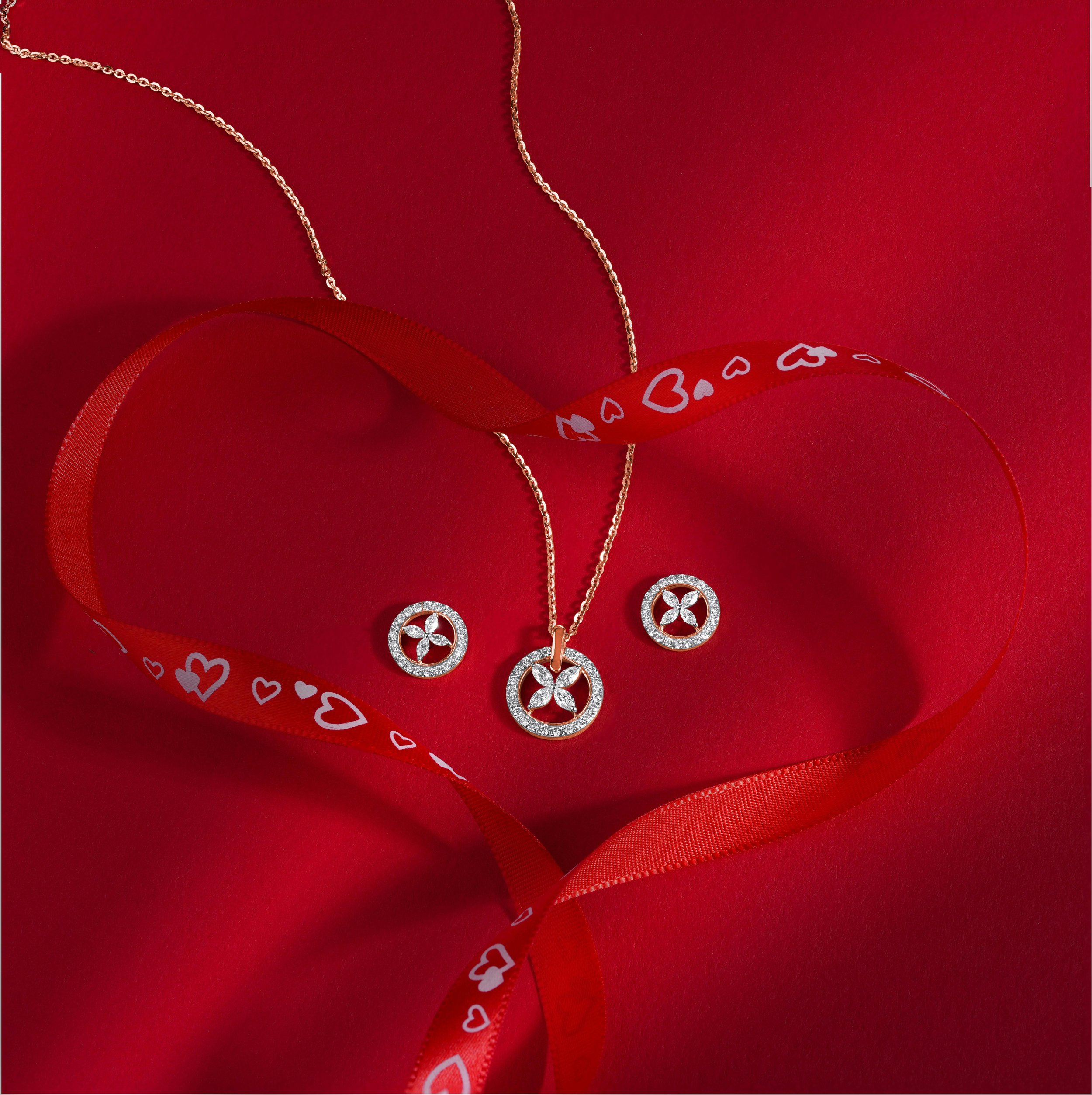 Gold necklace and earrings with circular pendants decorated with small diamonds, displayed on red background with a red ribbon featuring white hearts and card suit symbols, arranged to form a heart shape.