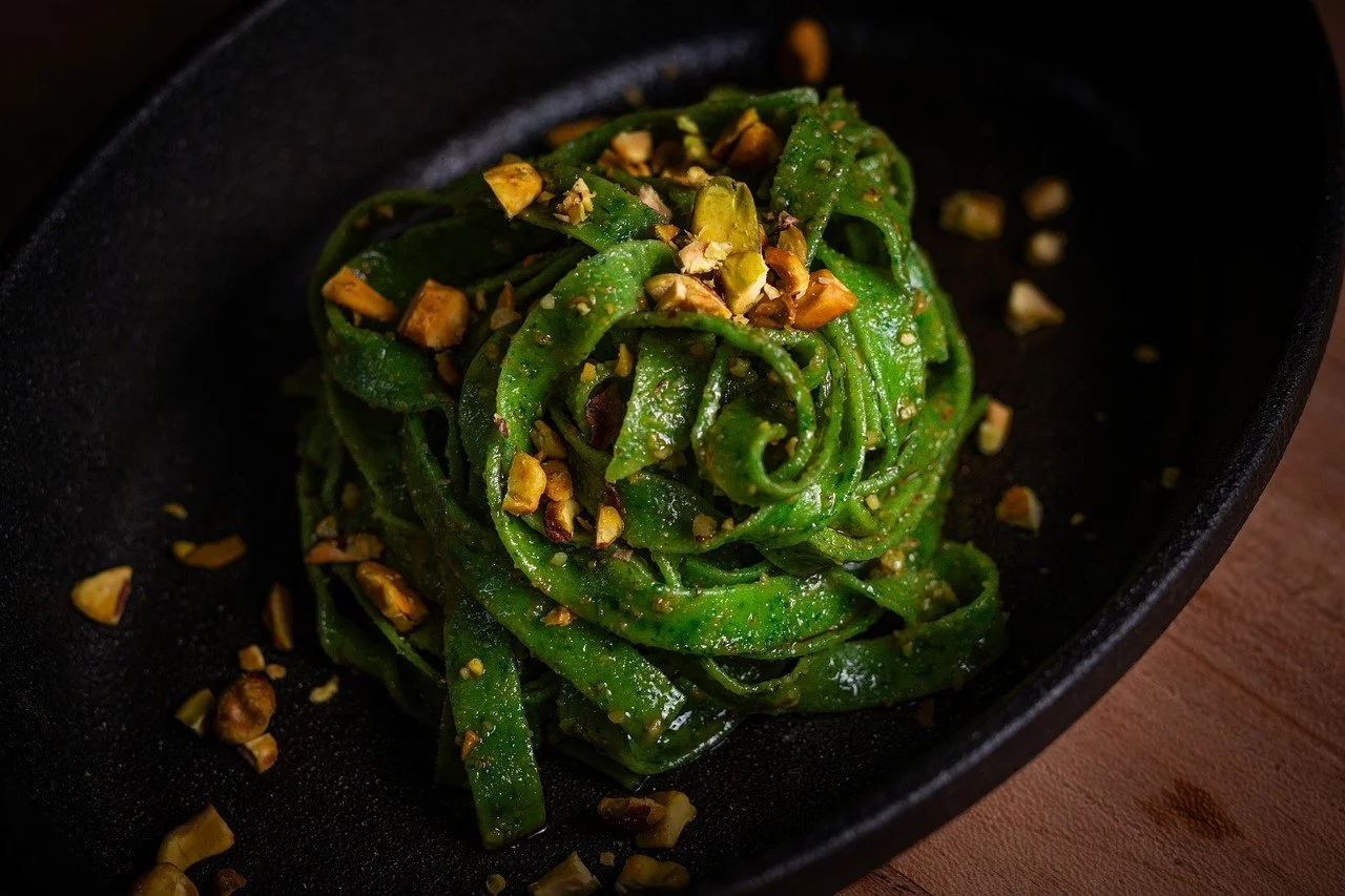 A black bowl containing green seaweed salad topped with chopped pistach nuts.