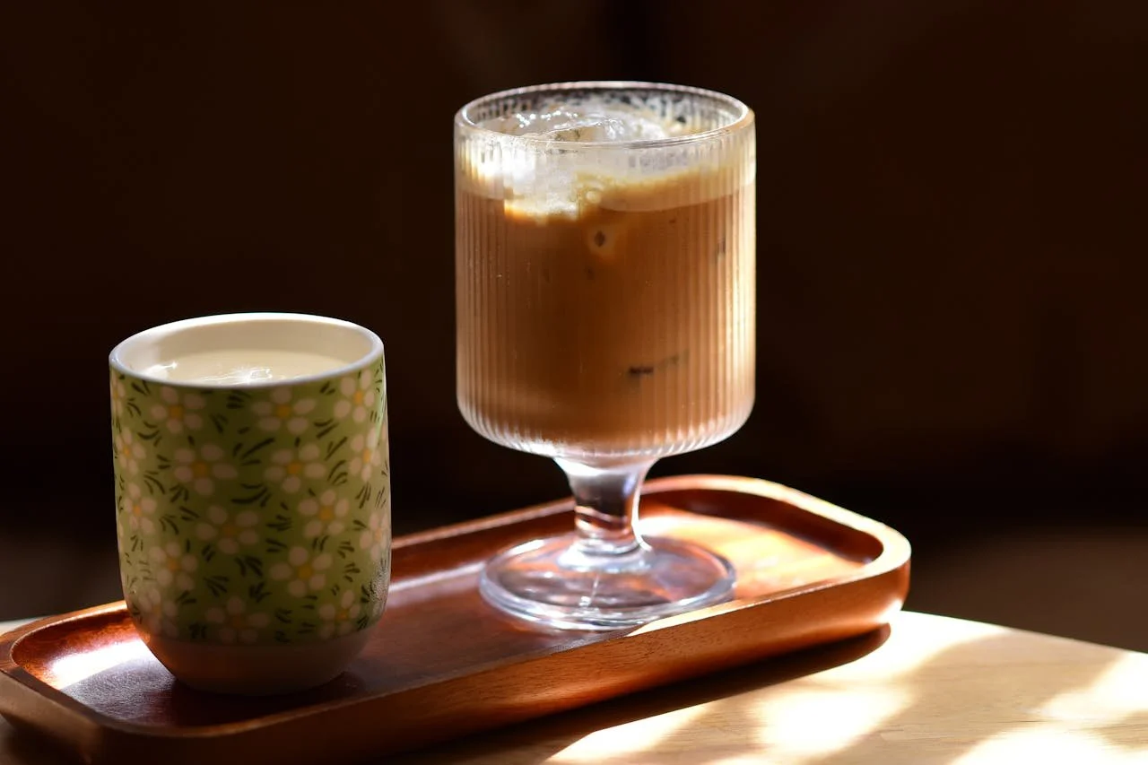 An iced coffee in a tall glass and a cup of milk in a floral patterned mug on a wooden tray.
