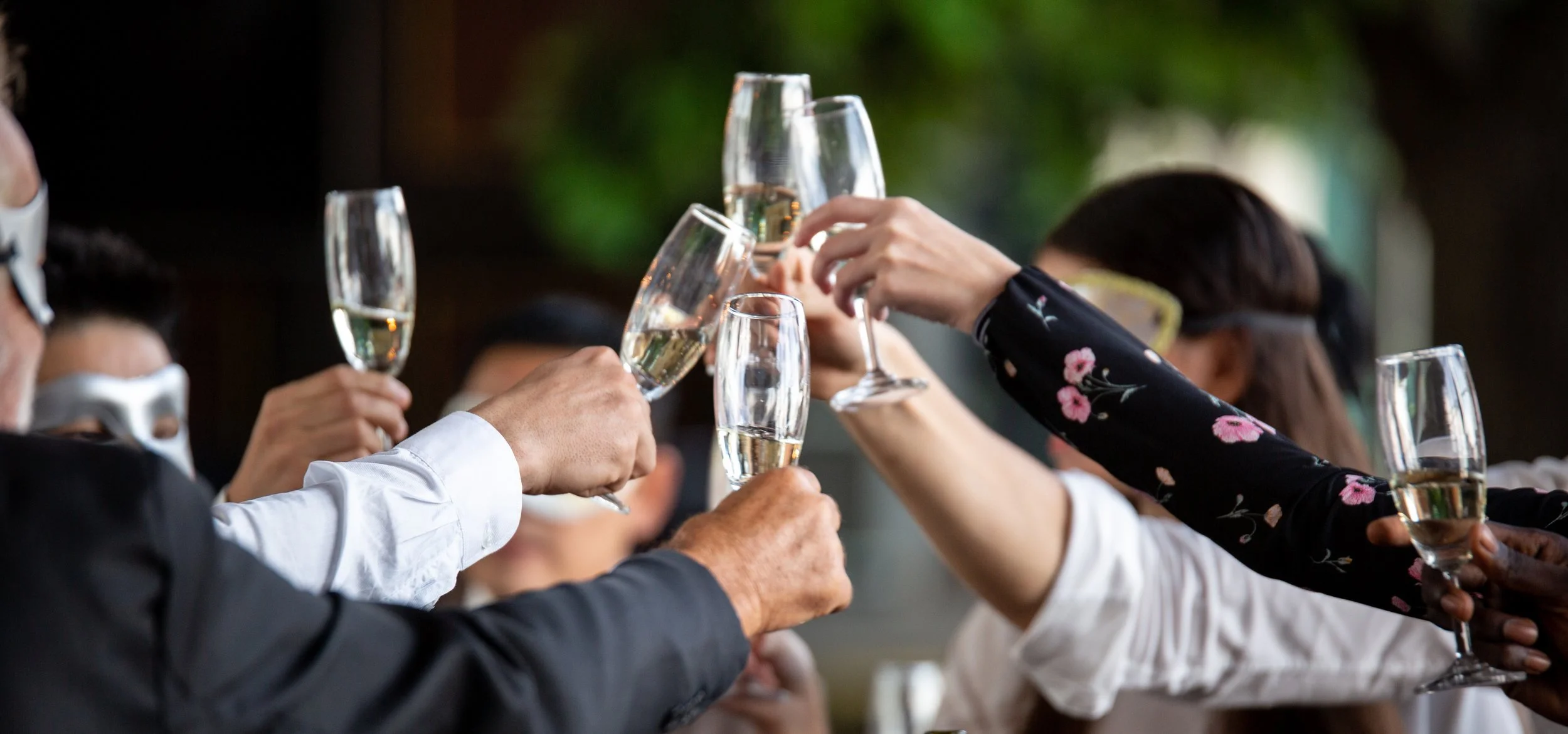 People in formal attire with face masks toasting with champagne glasses during a celebration.