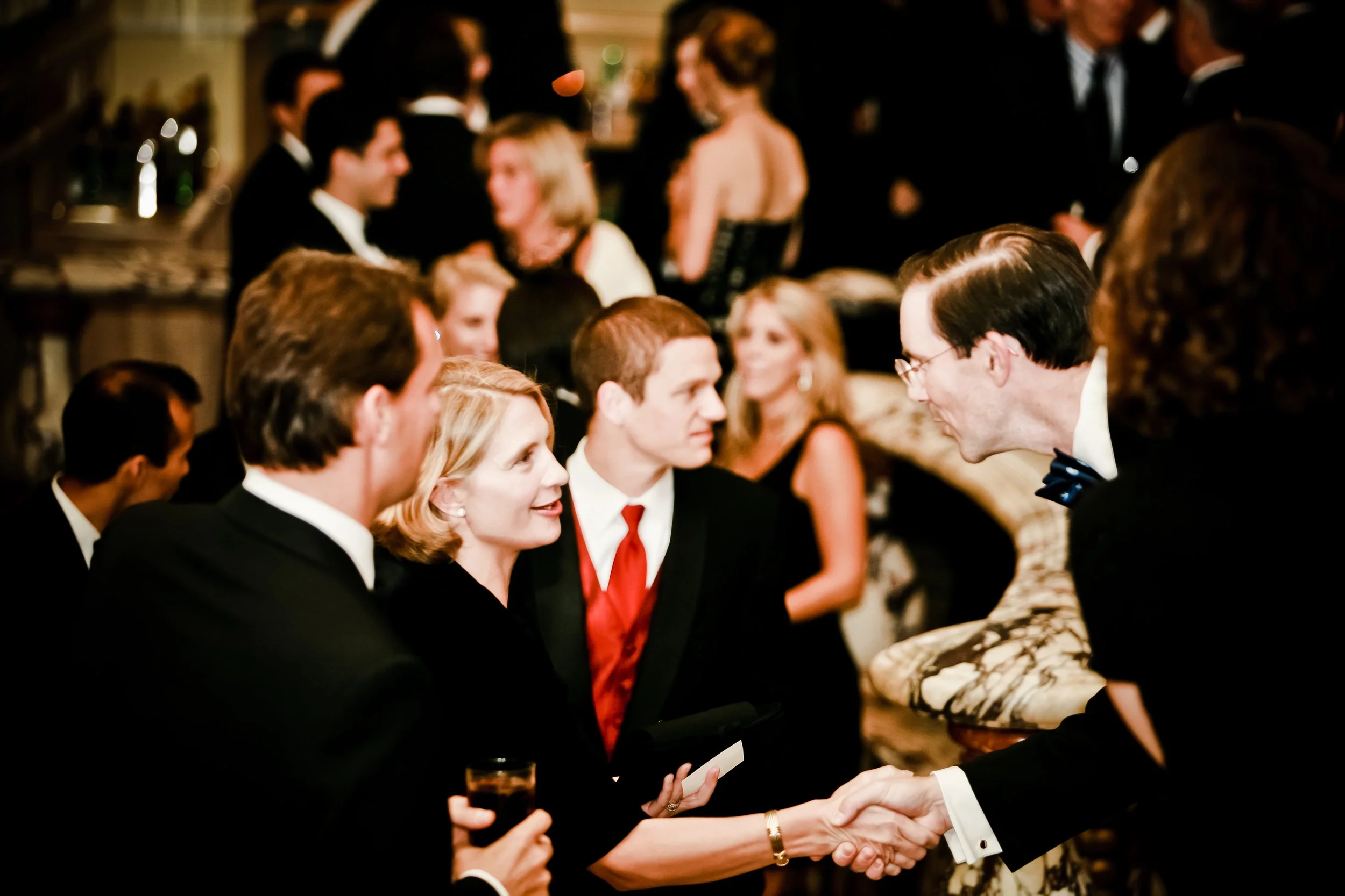 People in formal attire socializing at an elegant event, shaking hands and engaging in conversation.