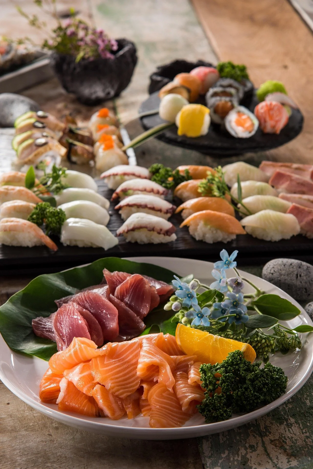 Assorted sushi and sashimi on plates with flowers and decorative stones.