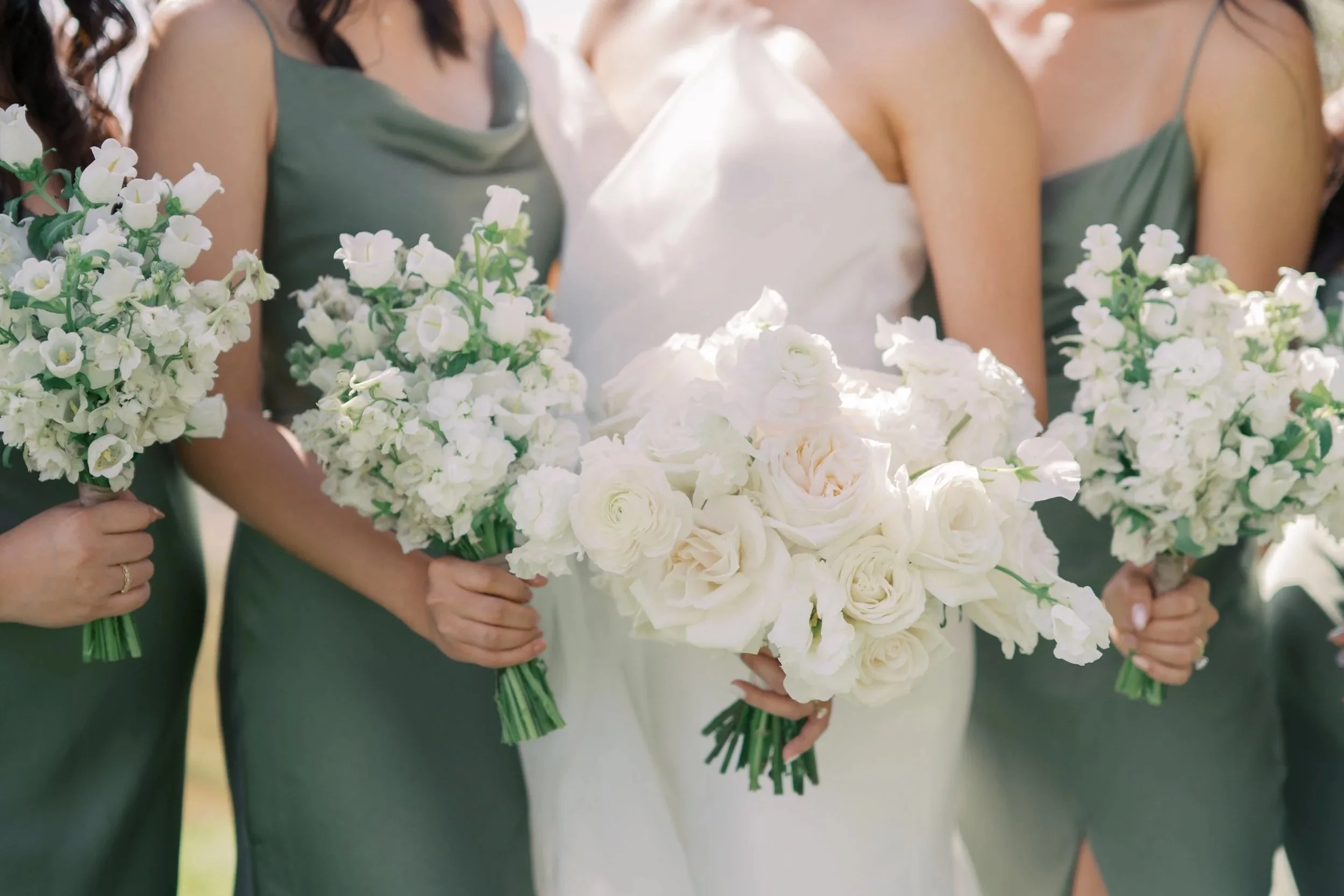 Close-up of a bride and bridesmaids holding white and cream bouquets at a wedding.