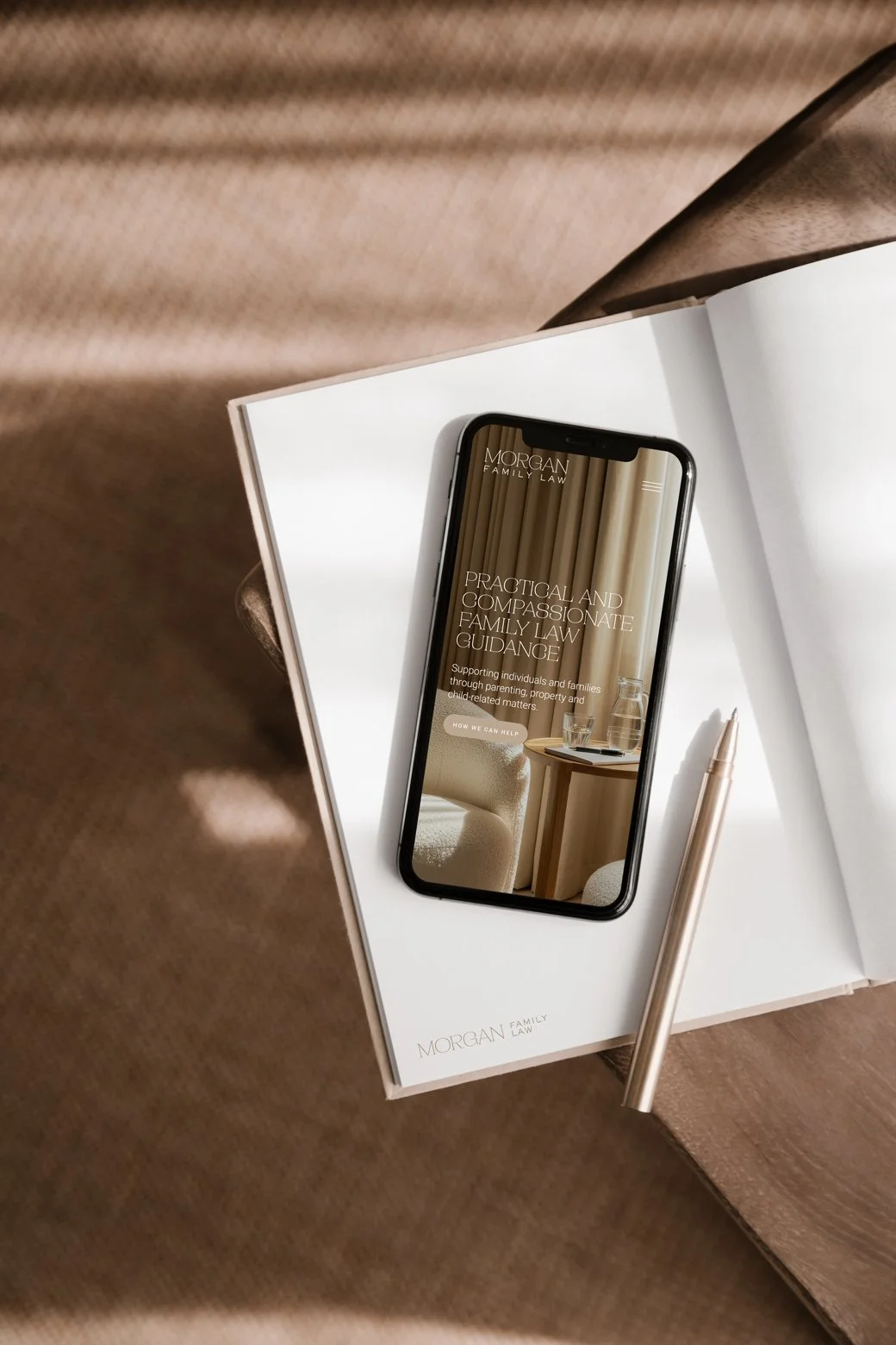 Open book with a smartphone displaying a law firm's website, a pen laying on the book, and a soft brown fabric surface.