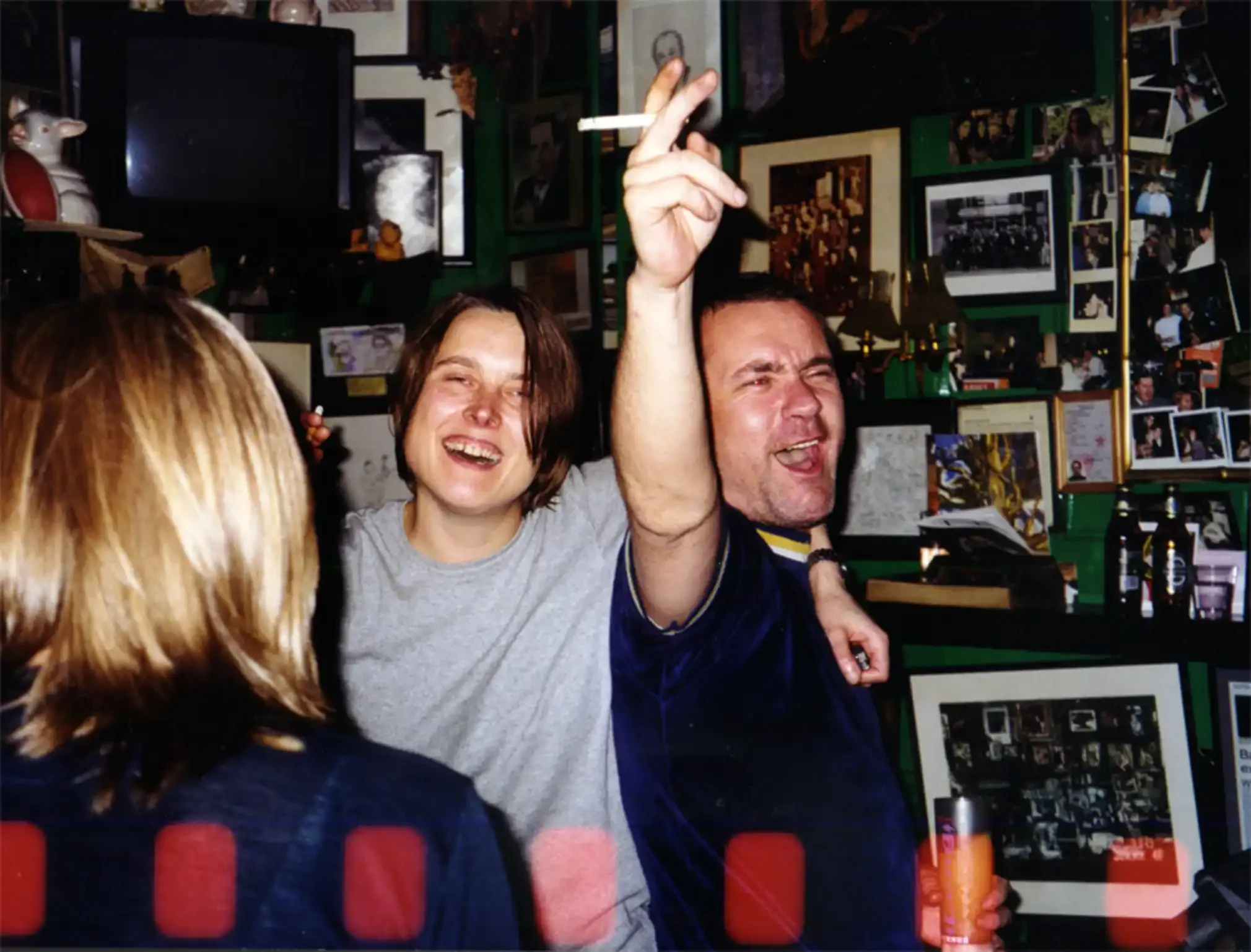 Group of friends enjoying a lively moment in a bar with framed photos and memorabilia on the wall.