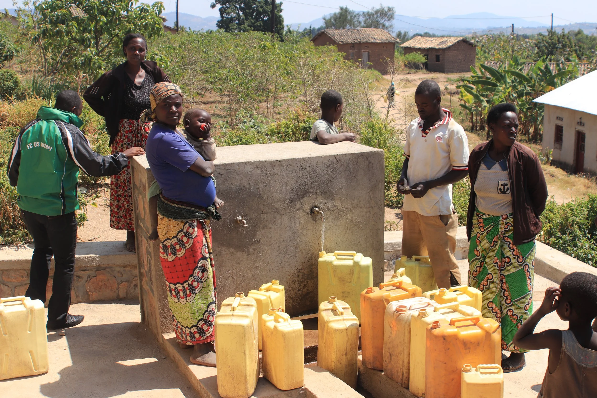 Des adultes et des enfants collectent de l'eau à une source d'eau dans le village de Nyundo (Rwanda), avec plusieurs jerricans jaunes et orange devant eux.