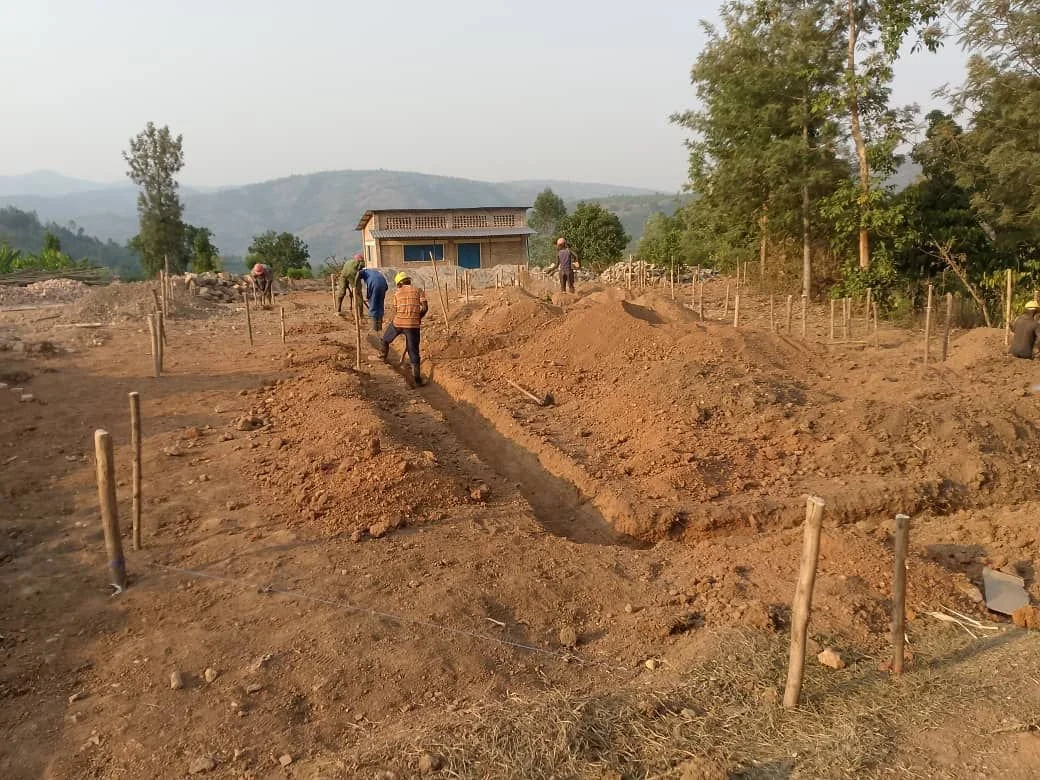 Des ouvriers construisent une terrasse en terre dans un champ avec des montagnes en arrière-plan.