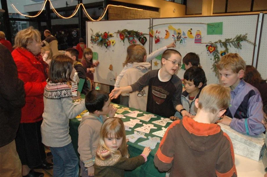 Group of children and adults participating in a craft fair, with holiday decorations and handmade ornaments on display.