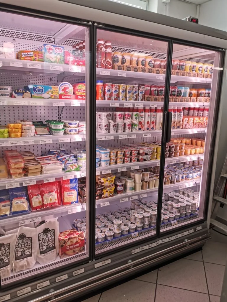 Réfrigérateur rempli de produits laitiers, yaourts, crèmes, fromages, et boissons dans une supérette.