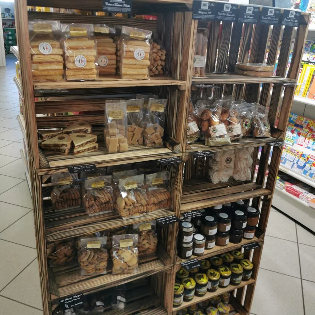 Étagère en bois avec des packs de biscuits, confitures, et autres produits alimentaires en vrac dans une épicerie.