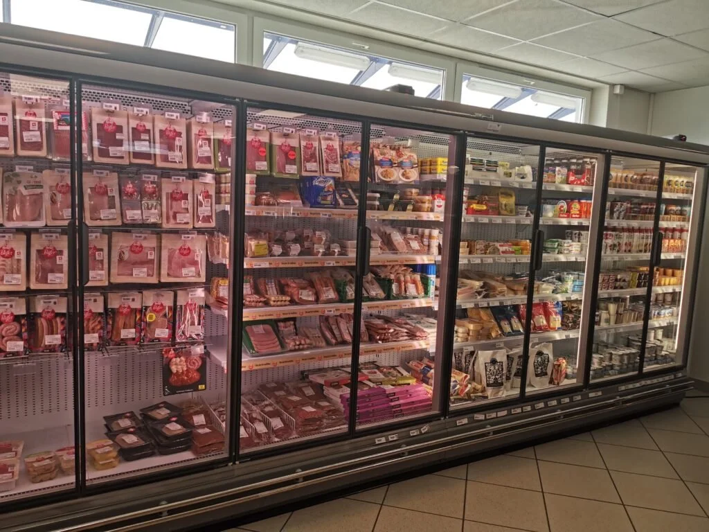 Une grande vitrine réfrigérée dans un supermarché contenant des produits de charcuterie, viandes et fromages.