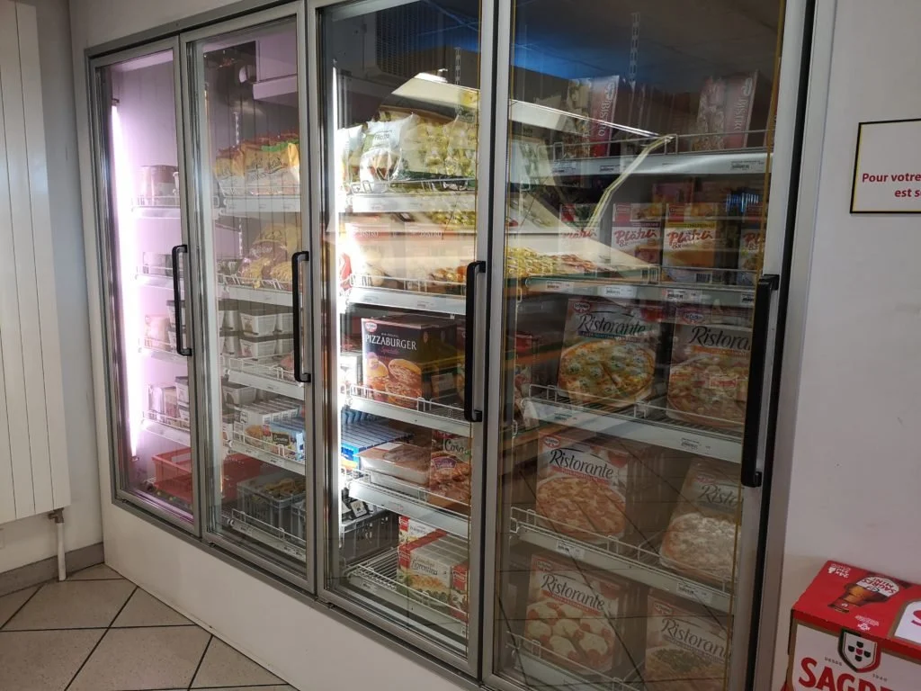 Un meuble réfrigéré contenant diverses pizzas congelées dans un supermarché.