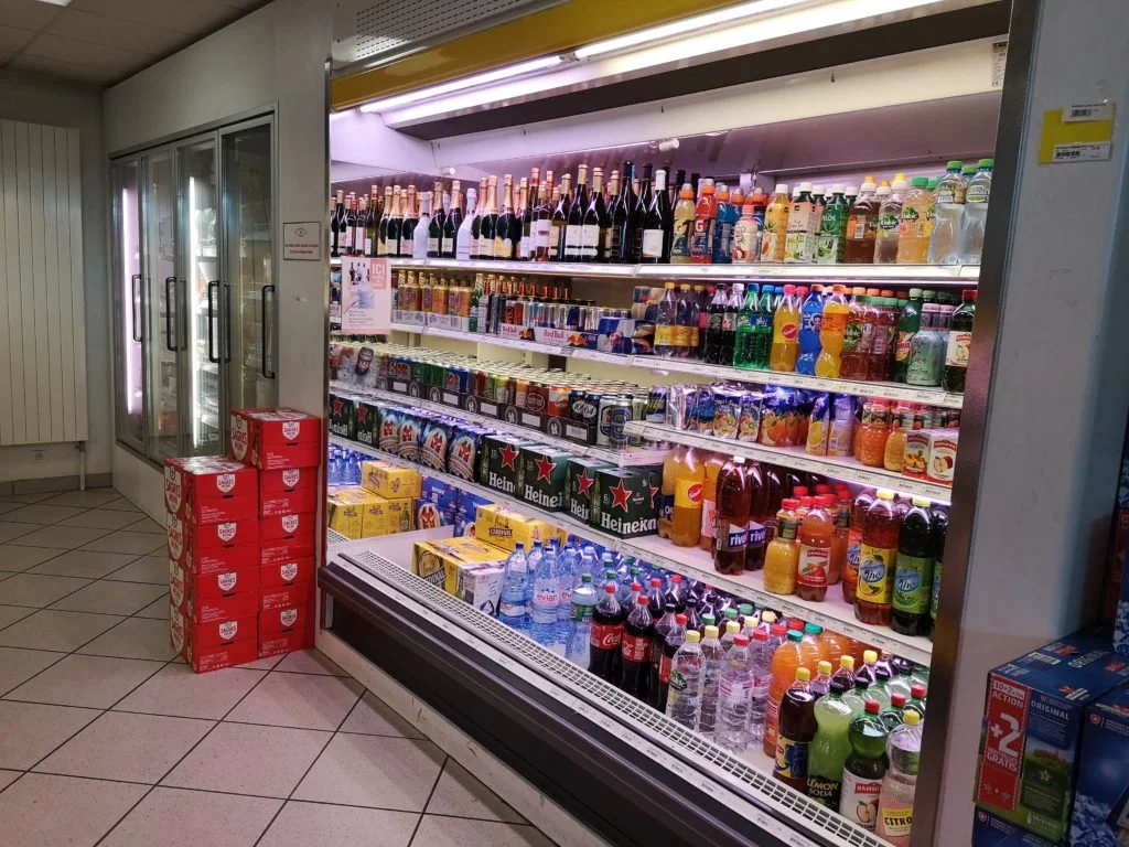 Rayonnage réfrigéré avec différentes boissons, dont des bouteilles de vin, des sodas, et des eaux, dans une épicerie.
