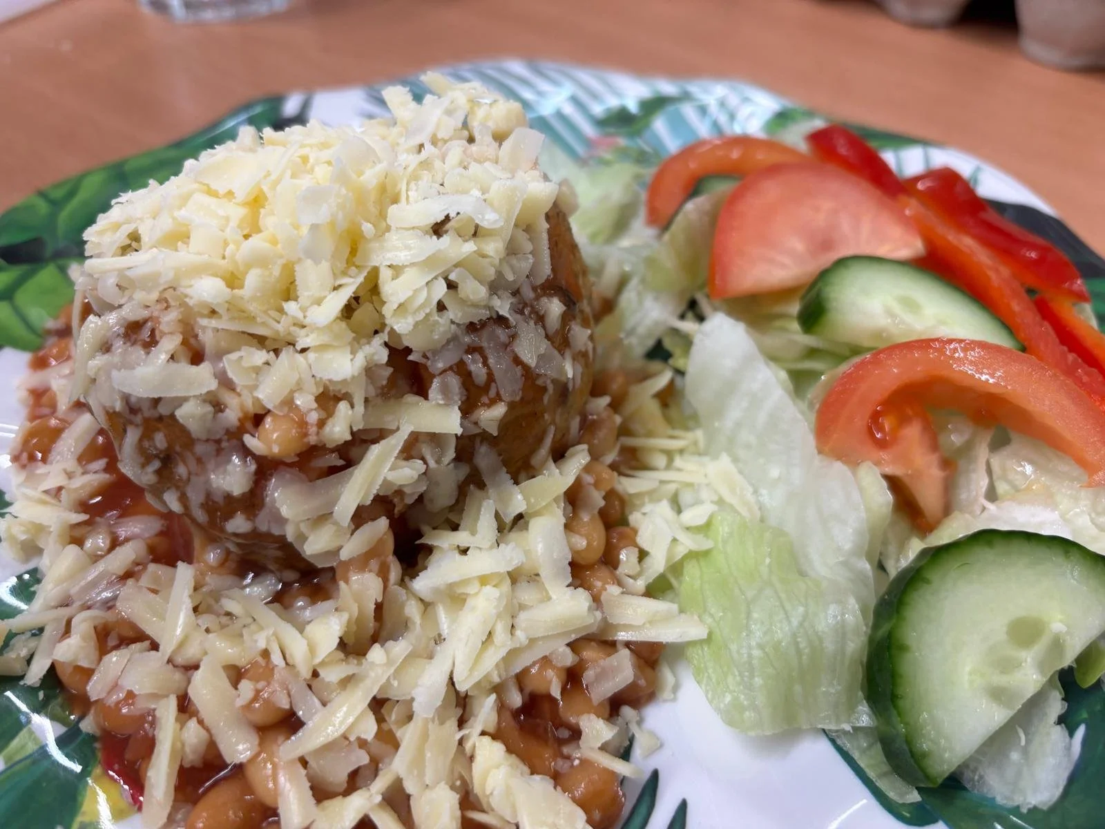 A plate with a baked enchilada topped with shredded cheese, alongside a side of mixed salad with sliced cucumbers, tomatoes, and lettuce.