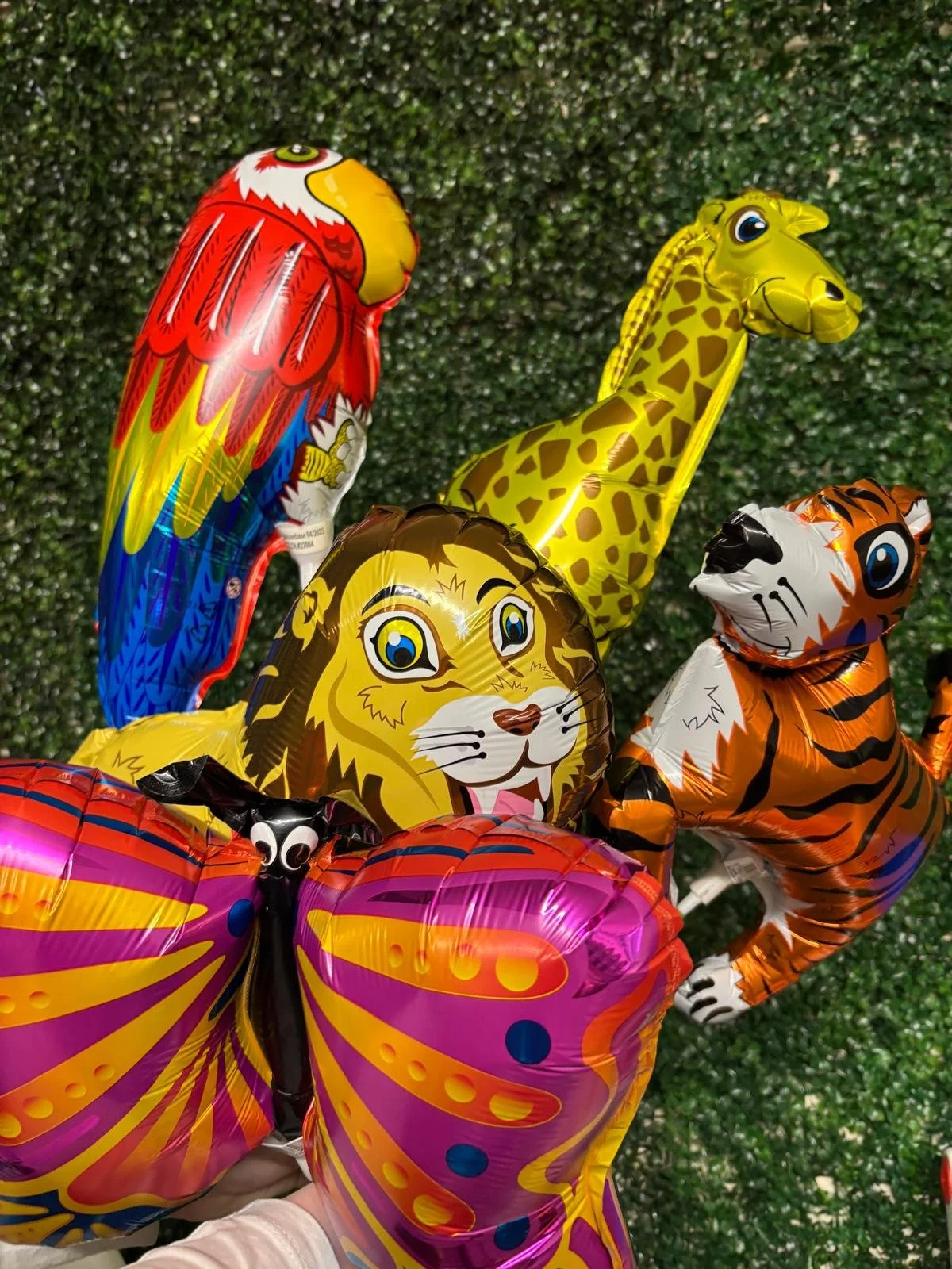 Colorful animal-shaped and butterfly-shaped foil balloons held in a person's hand against a green background.