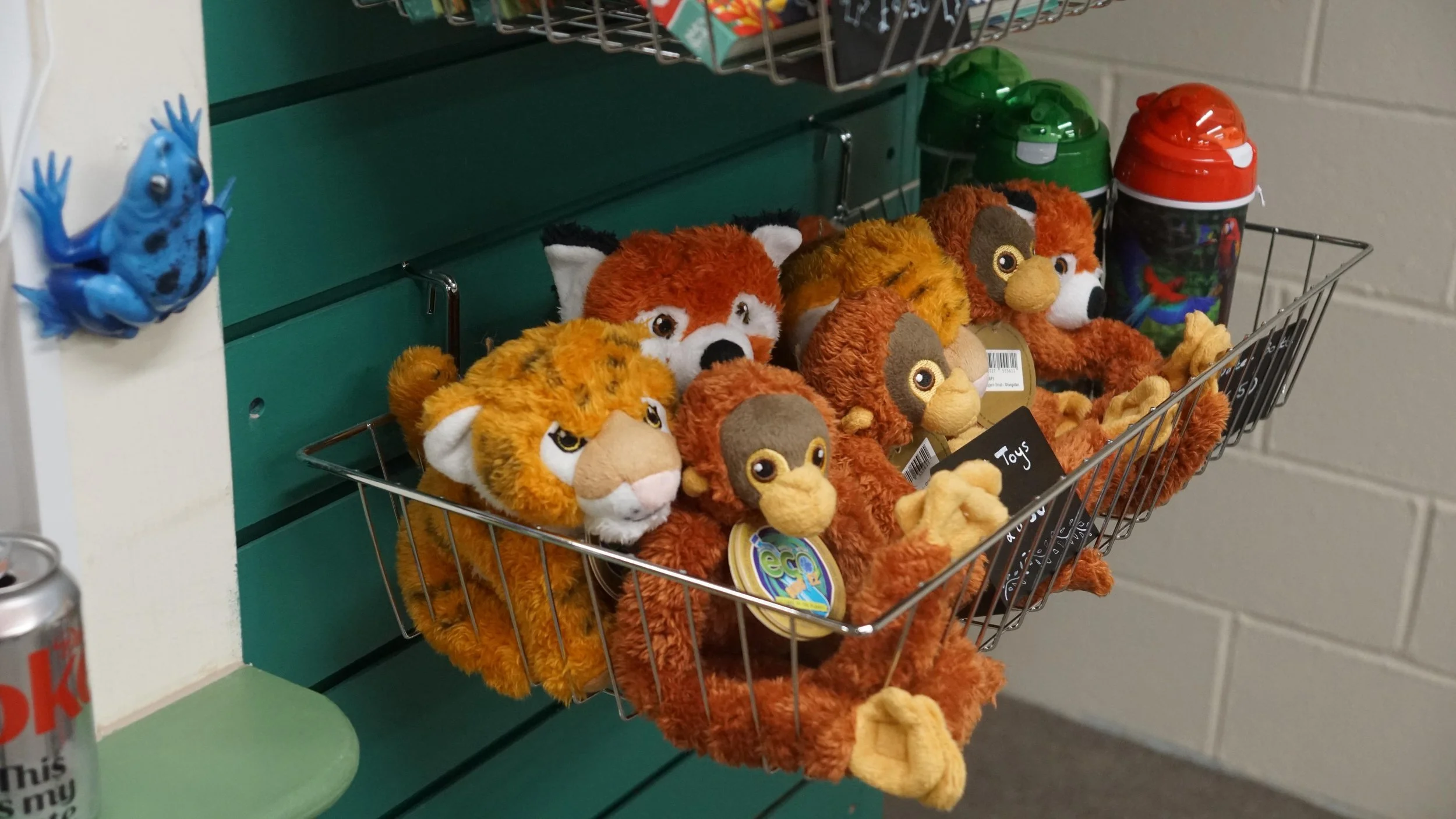 A wire basket on a green shelf filled with plush lion and monkey toys, with toy containers in the background.