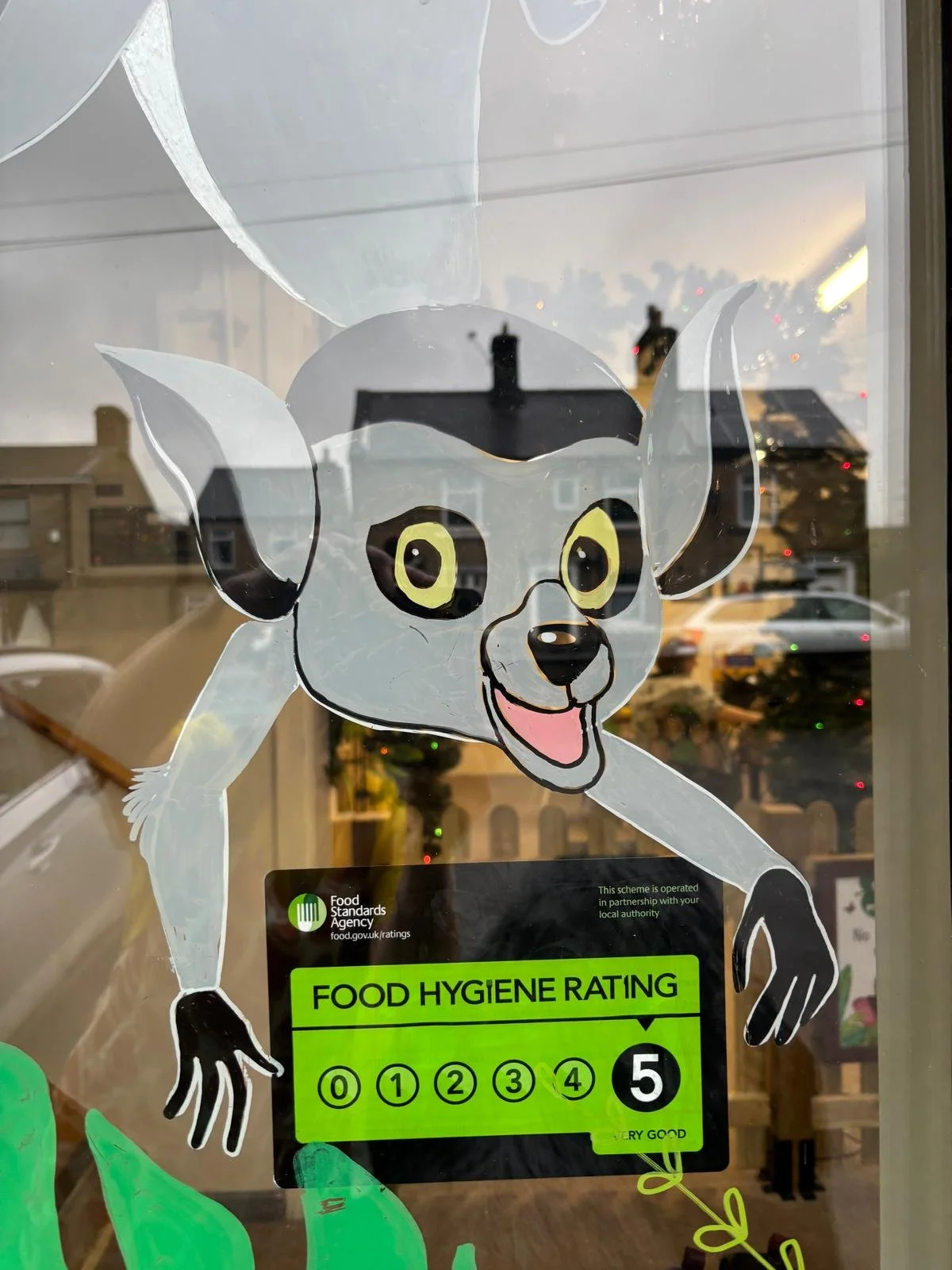 A window decal of a cartoon alien dog with large ears, yellow eyes, and a friendly expression. The decal includes a food hygiene rating sticker with a rating of 5, indicating very good cleanliness and safety standards.