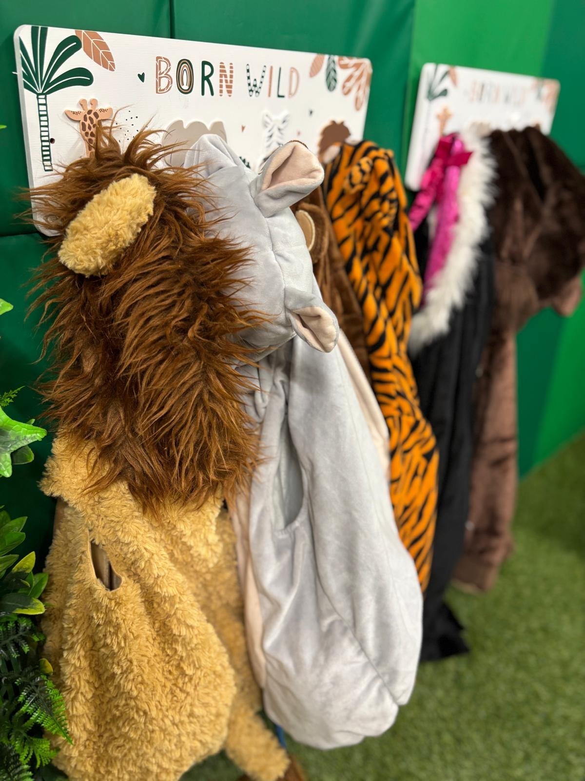 A display of various animal-themed hooded onesies hanging on hooks with signs that say 'Born Wild' in a store.
