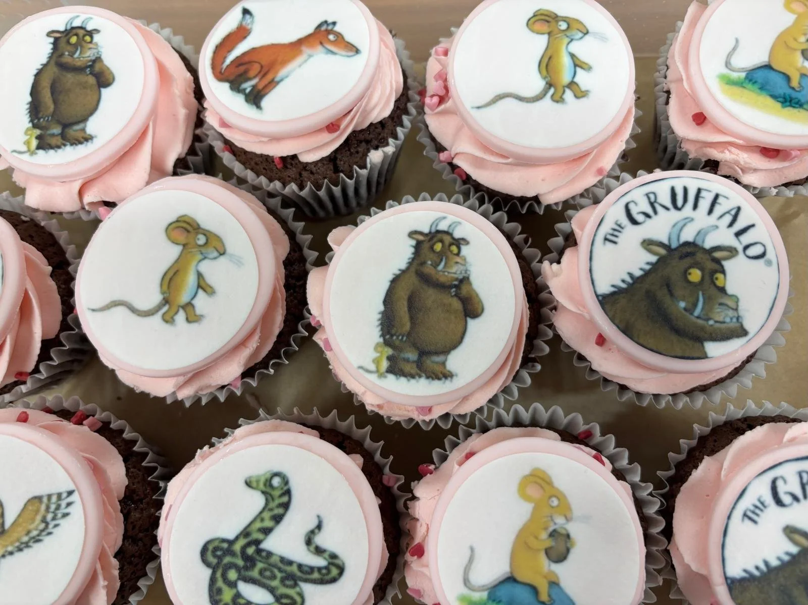 Cupcakes with pink frosting and edible images from the animated series 'The Gruffalo,' featuring various characters including a mouse, snake, and Gruffalo.