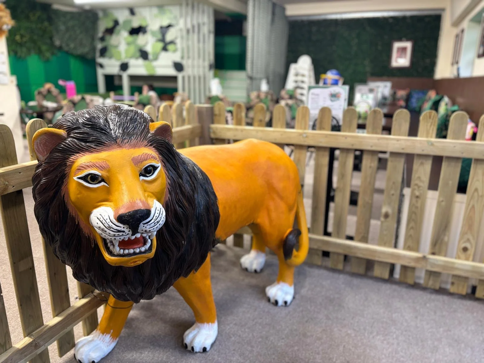 Plastic lion sculpture inside a fenced area, in a play area for children.