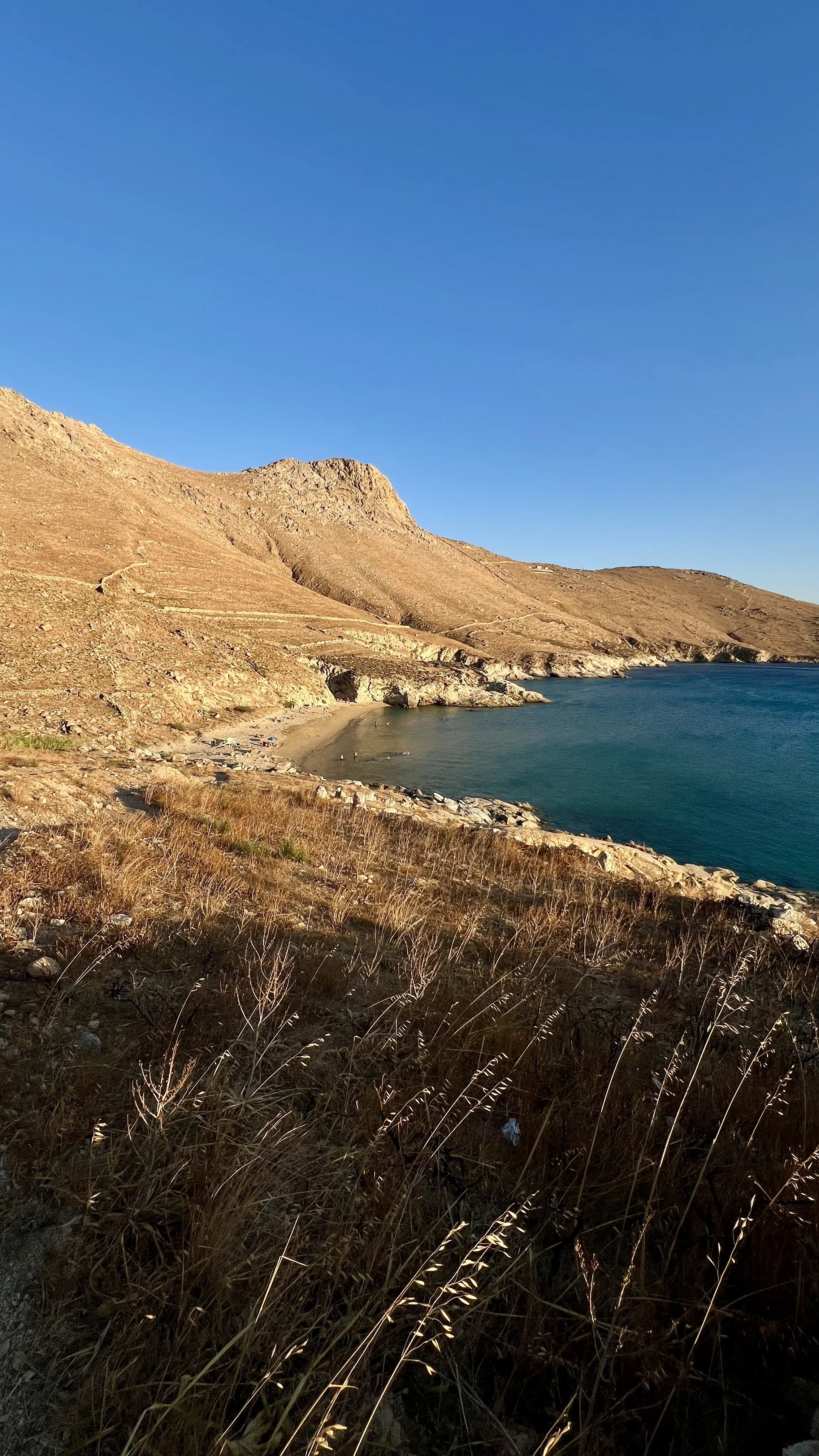 A coastal landscape with a mountain, a sandy beach, and the ocean under a clear blue sky.