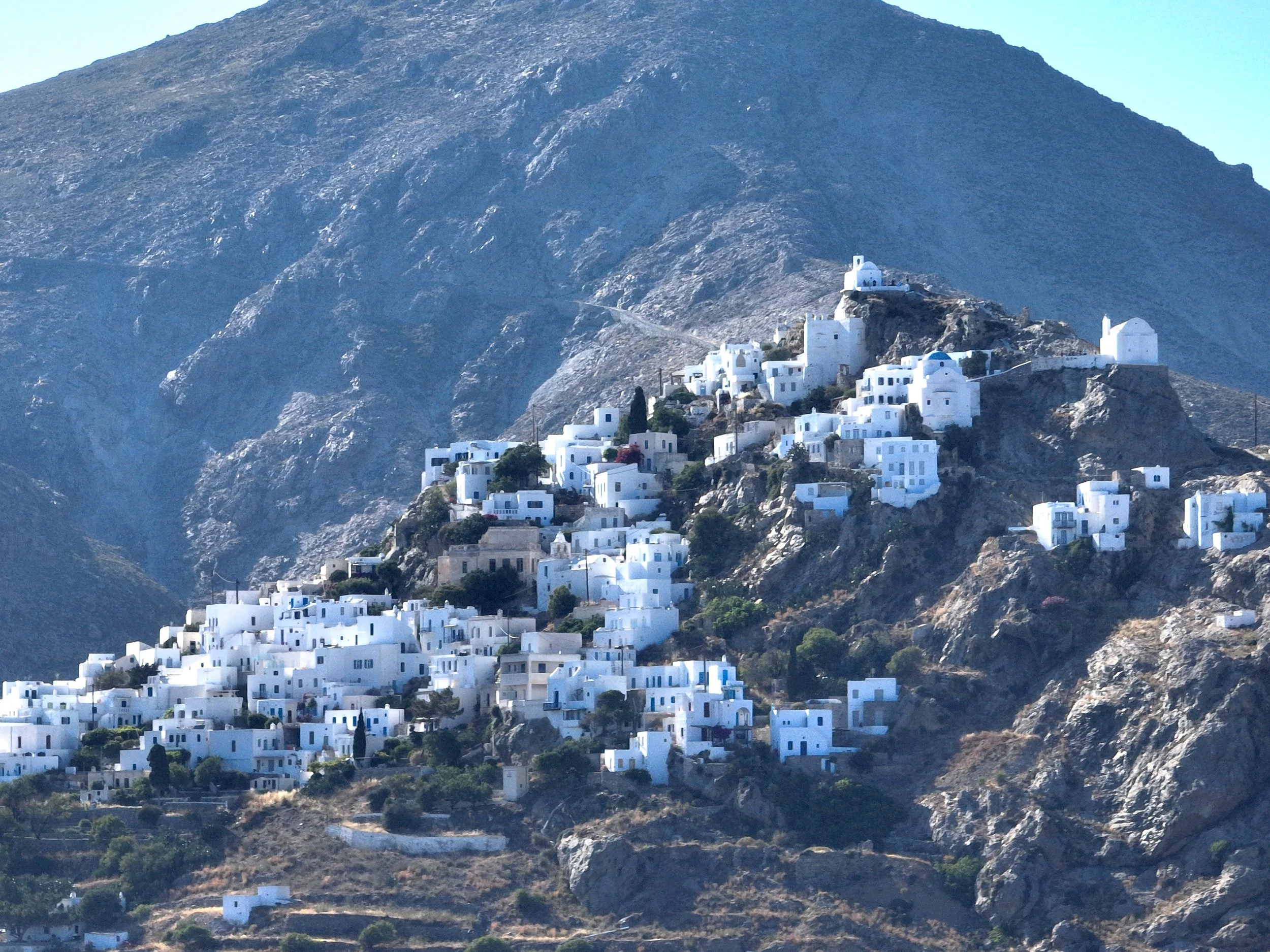 Cliffside village with white buildings on a steep hillside and mountain background.