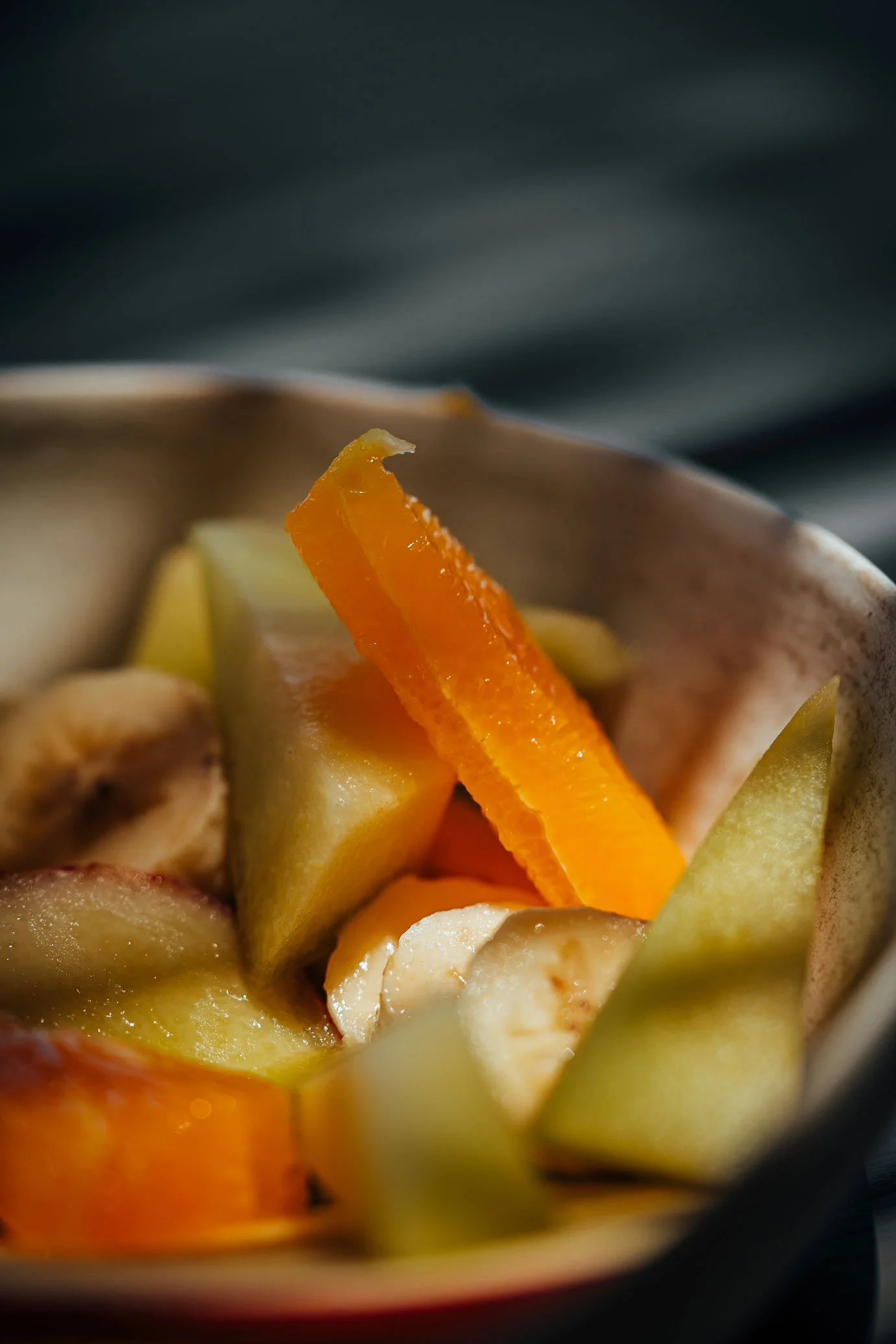 Close-up of a bowl containing fresh sliced fruits including bananas, oranges, and green melon.