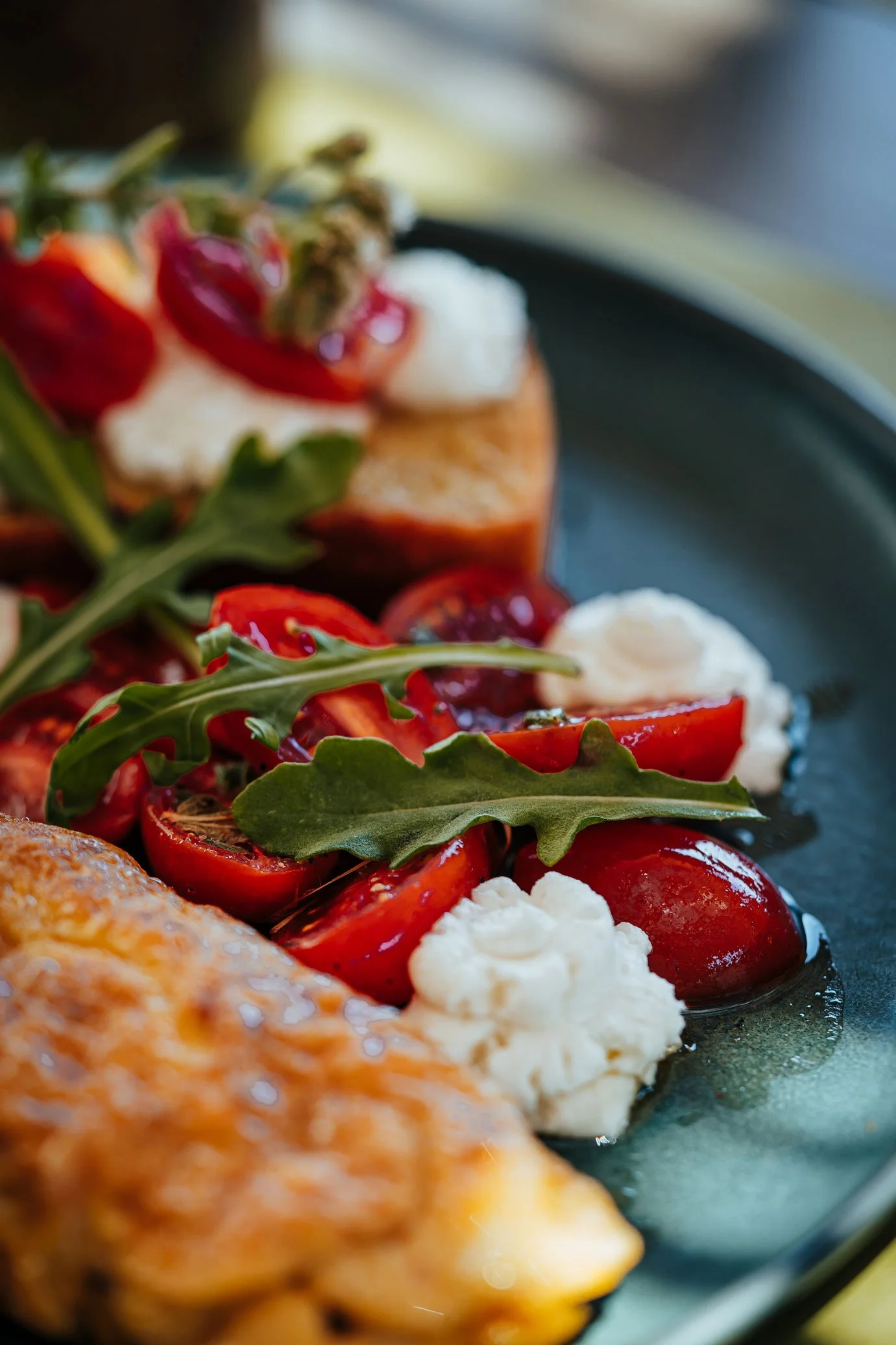 Close-up of a plate with cherry tomatoes, arugula, and dollops of cheese or cream alongside a crispy food item.