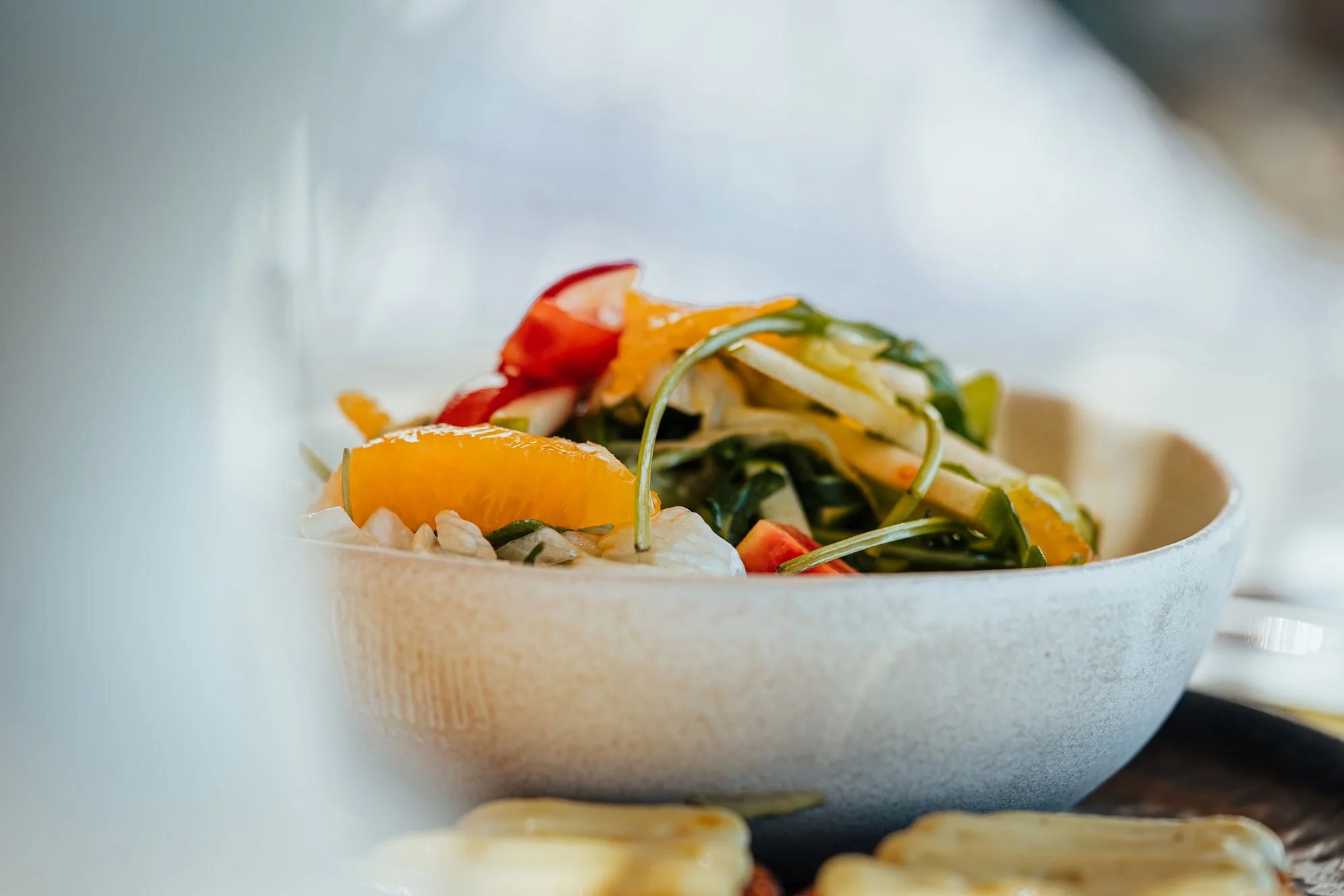 Fresh vegetable salad with cherry tomatoes, orange slices, and mixed greens in a white bowl.