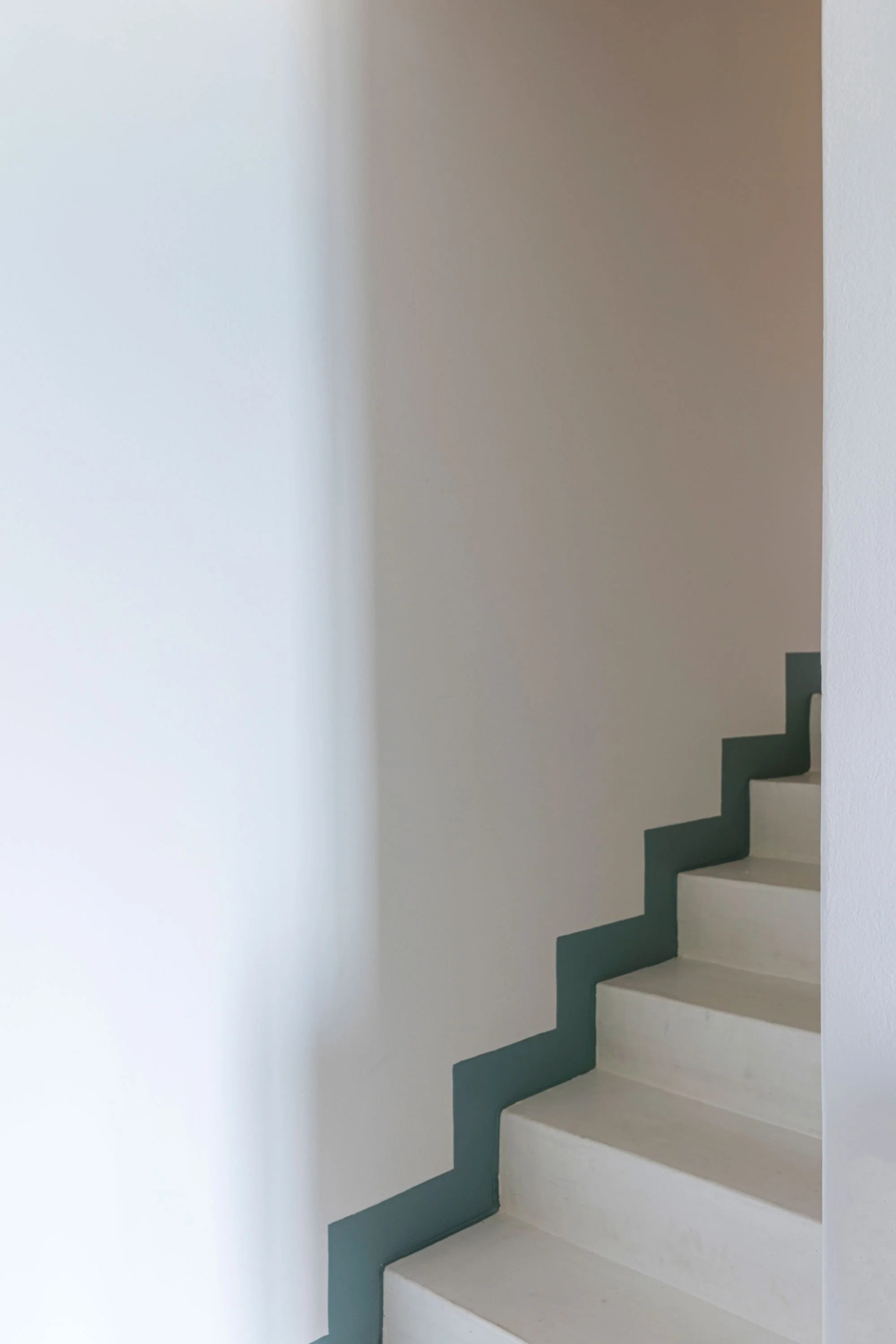 A stairway with white steps and a dark green zigzag railing against white walls.
