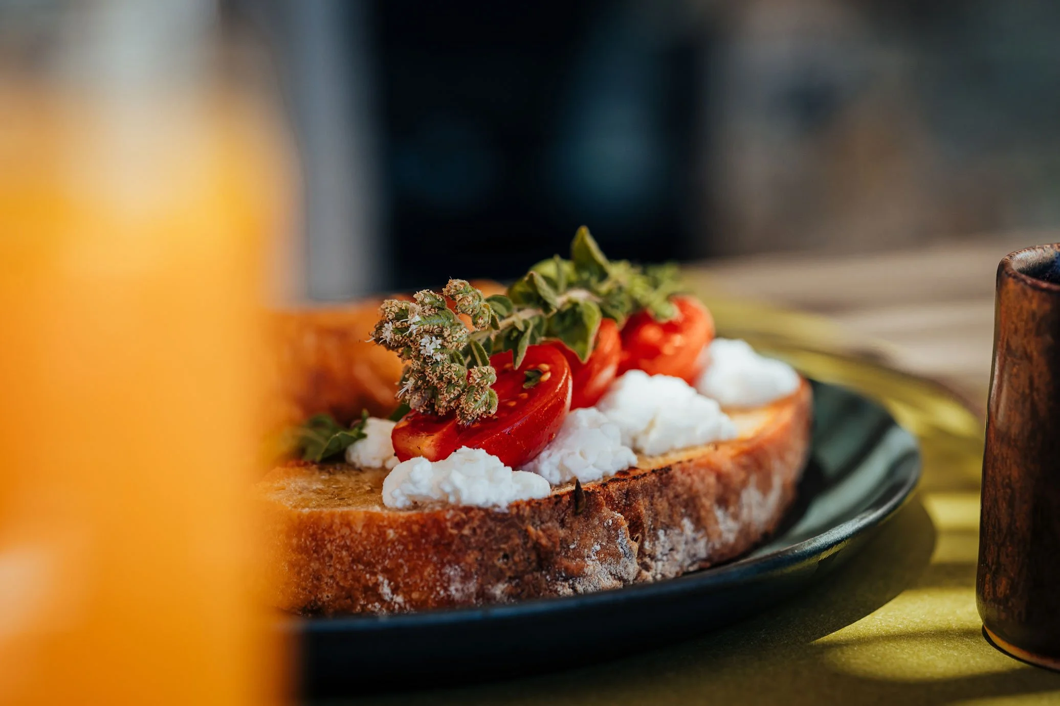 Close-up of a slice of toasted bread topped with cherry tomatoes, fresh herbs, and cheese, on a dark green plate.