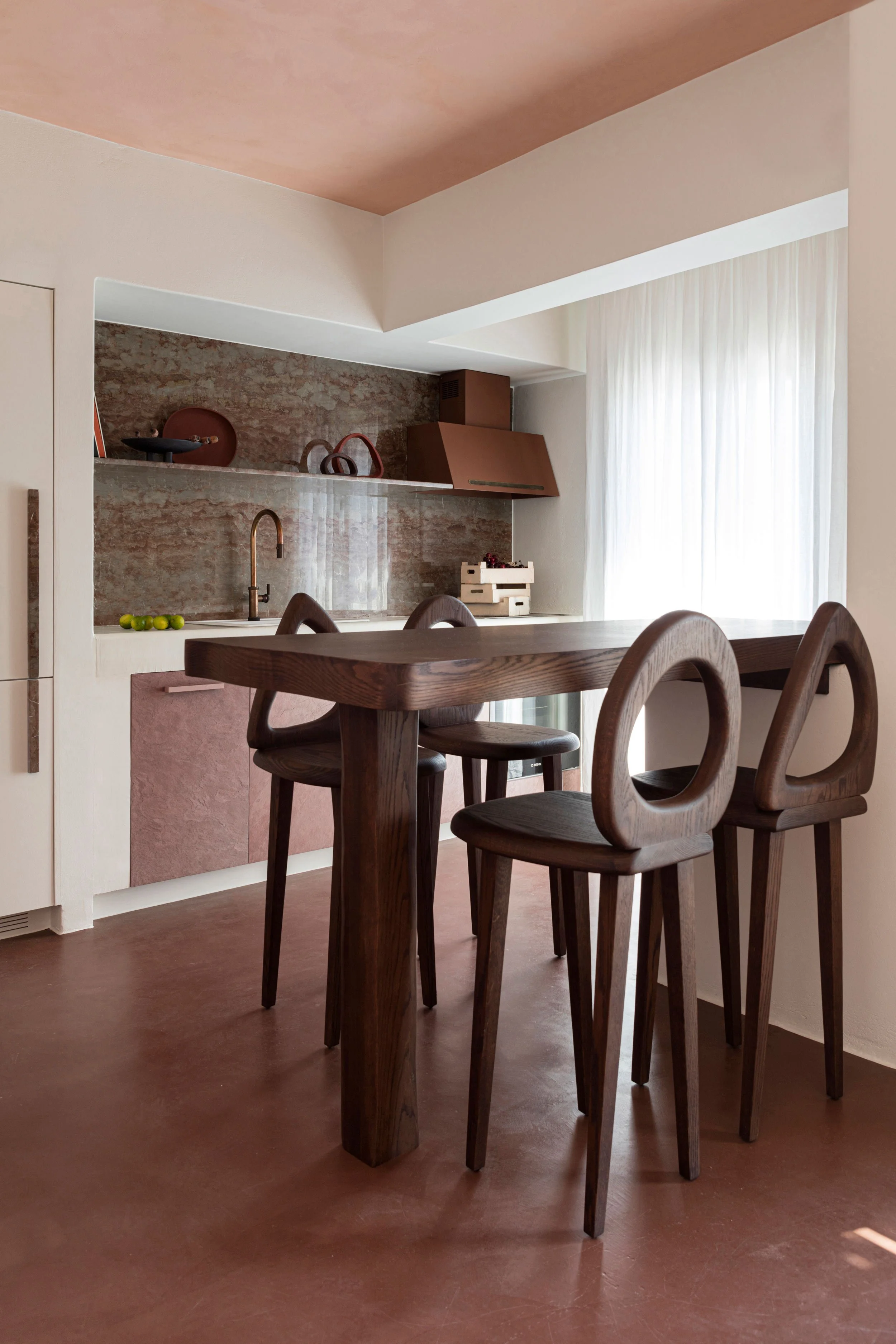 Modern kitchen with a dark wooden dining table and four matching chairs, a marble backsplash, and light curtains on a window.
