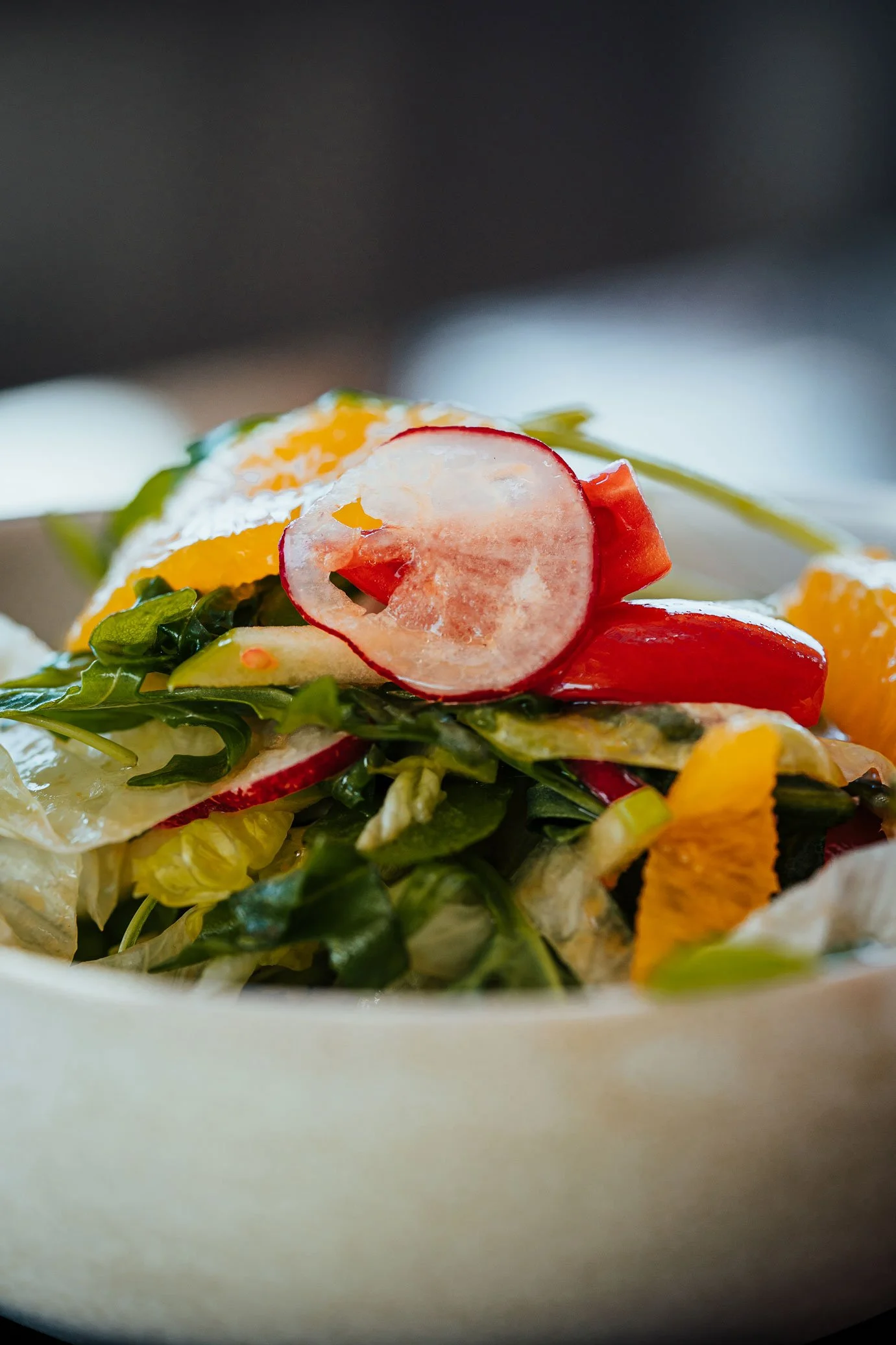 Close-up of a fresh mixed vegetable salad in a white bowl, including radishes, cherry tomatoes, lettuce, and bell peppers.