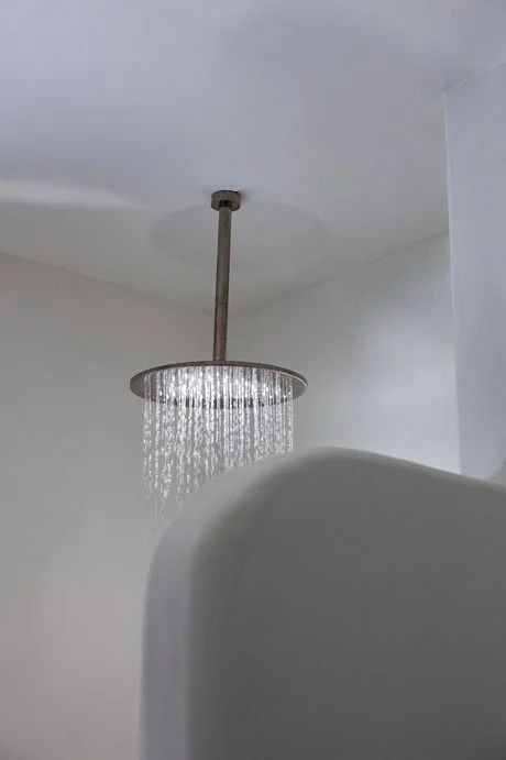Close-up of a modern showerhead with water flowing, mounted to a white ceiling in a bathroom.