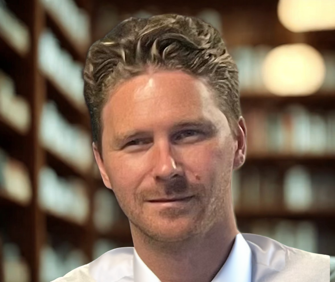 A teacher with short, brown hair, wearing a white shirt, standing in a library.